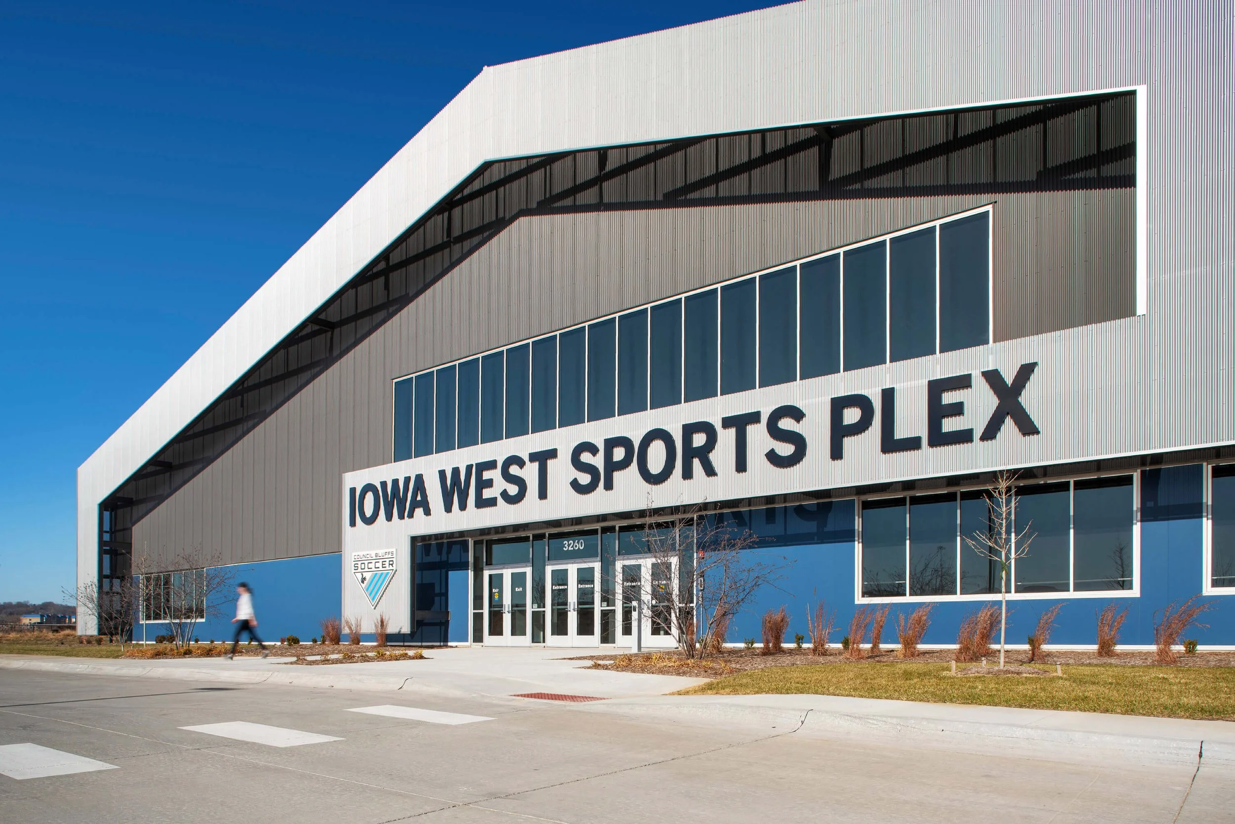Exterior view of the Iowa West Sports Plex building with signage and large windows, under a clear blue sky.