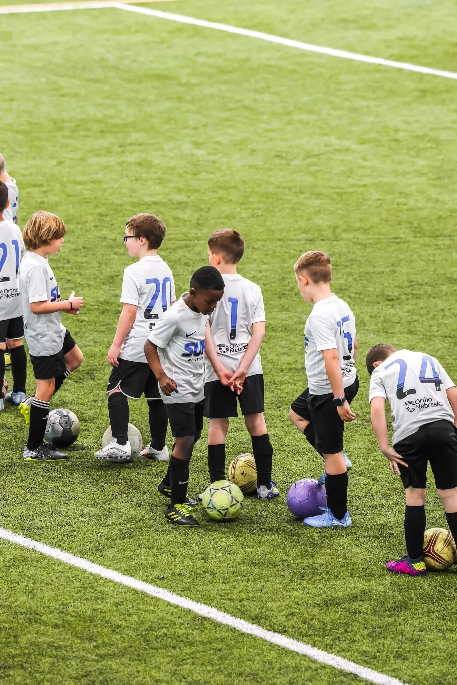 Young boys in sports jerseys standing on a soccer field with soccer balls.
