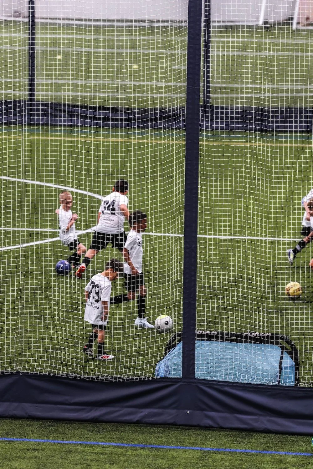 Children playing soccer inside a portable enclosed soccer goal on a grass field.