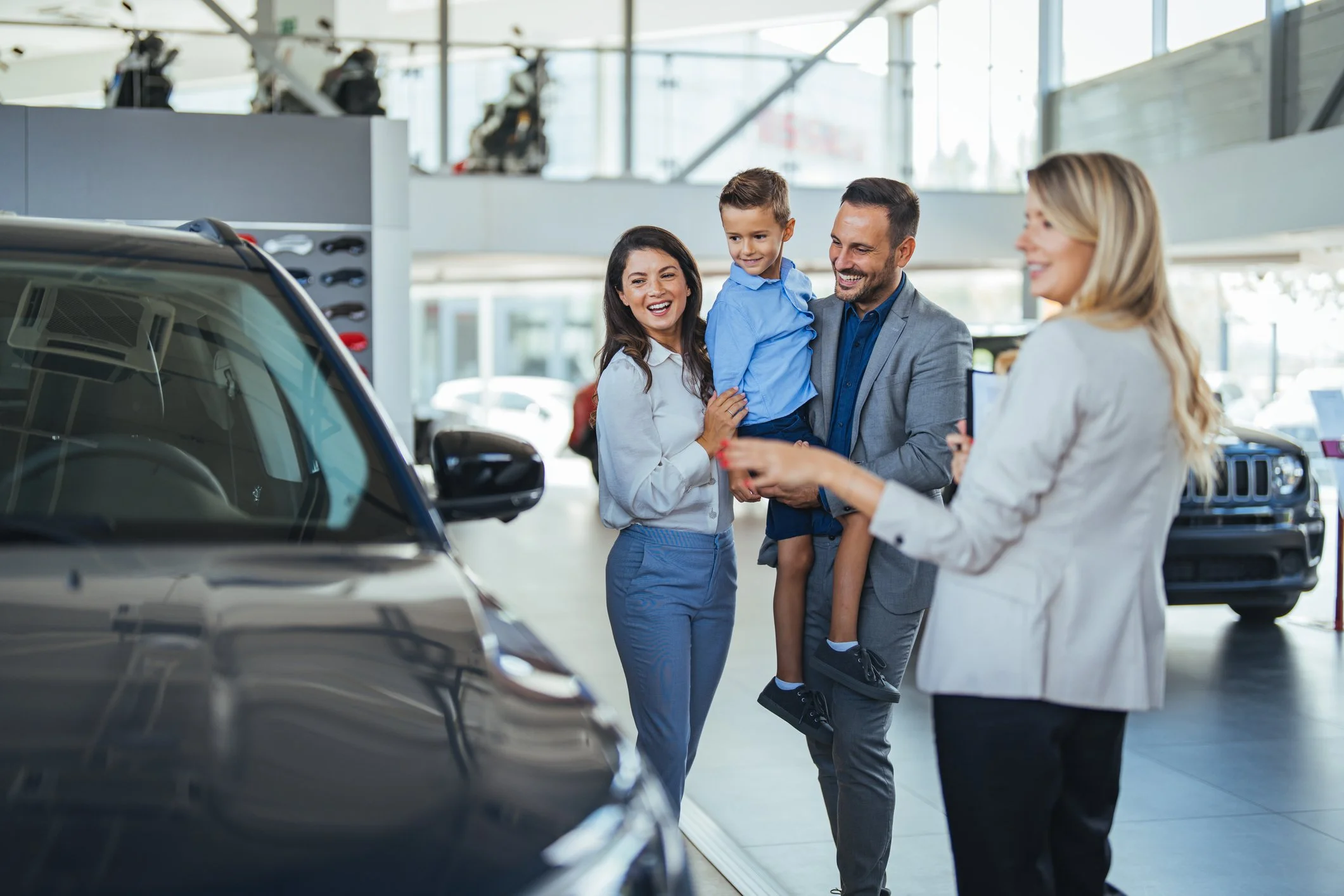 Happy family at a car dealership, taking new car delivery.