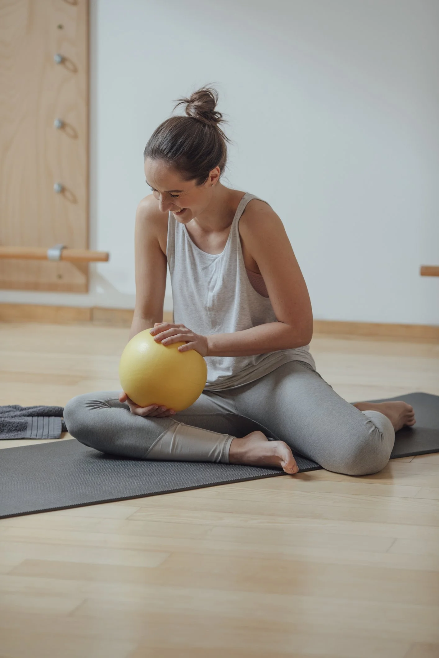 A woman practicing pilates matwork in Grayshott, holding a yellow exercise ball and smiling.