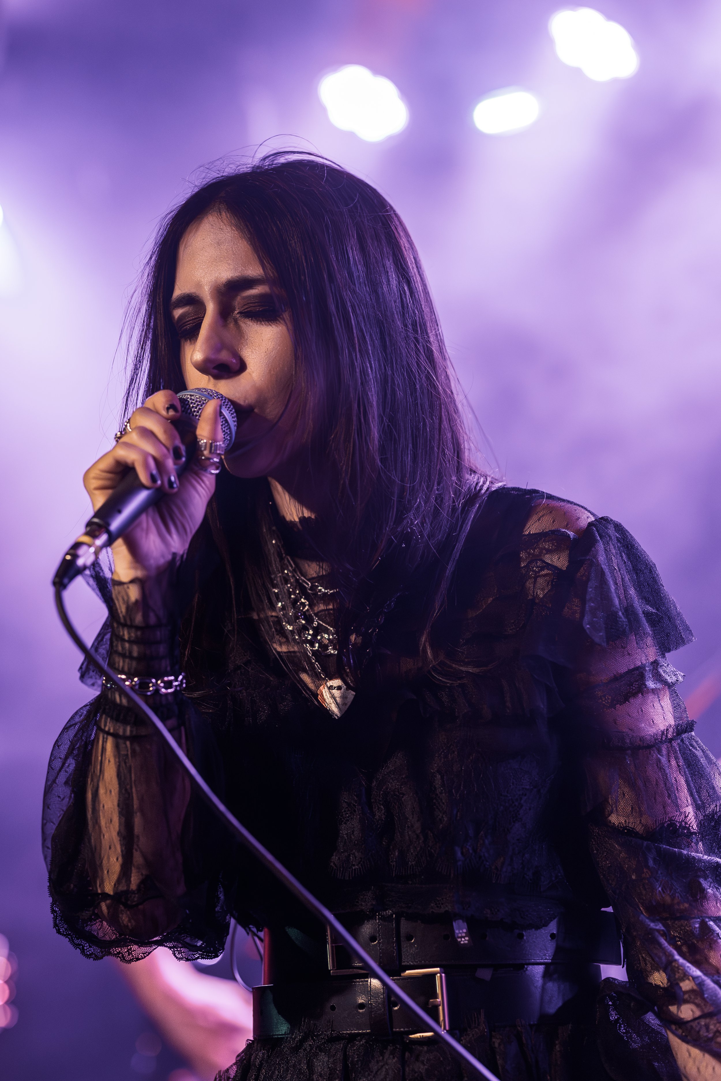 A woman singing into a microphone on stage with purple lighting.