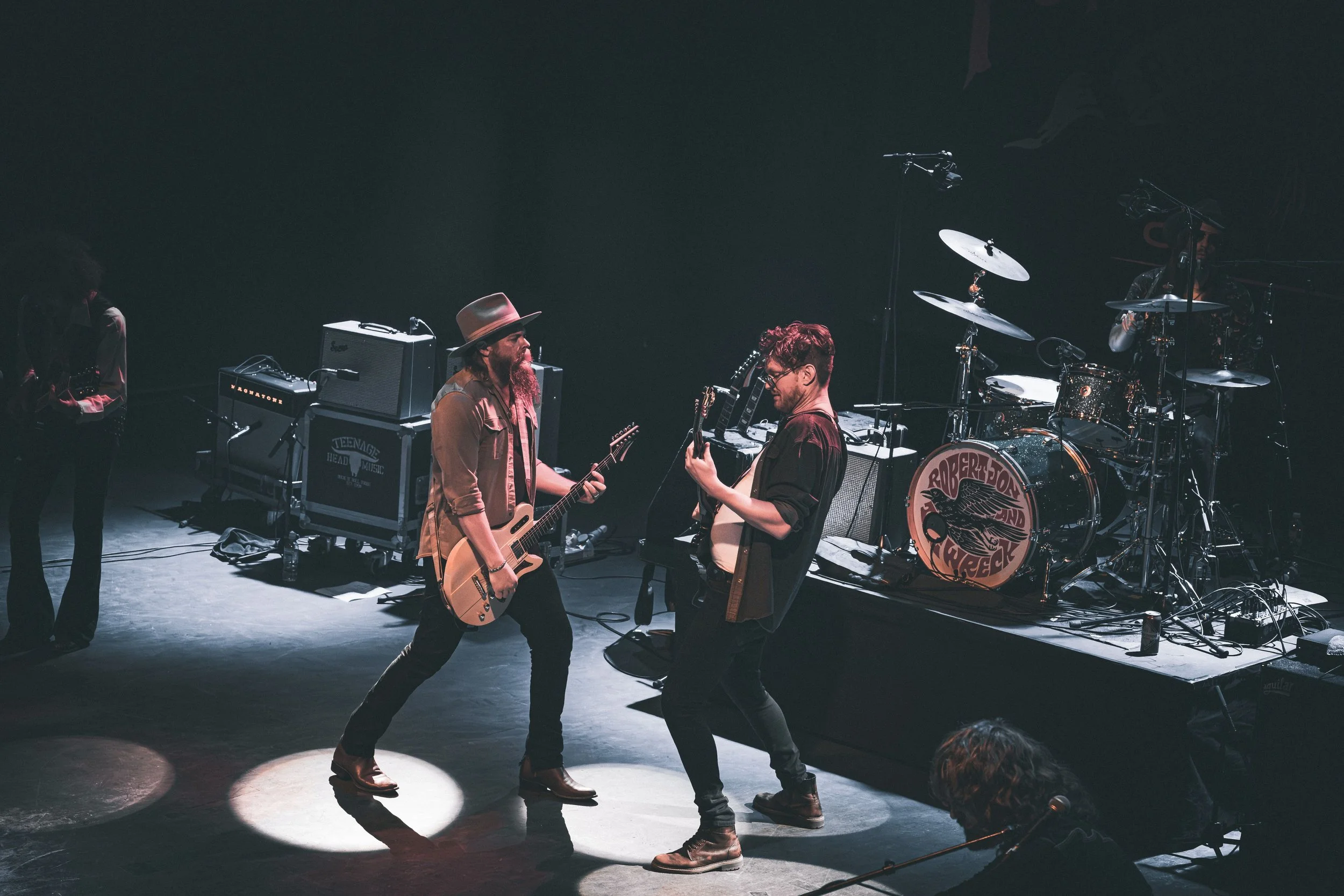Musicians performing on stage with guitars, drums, and amplifiers in a dark venue.