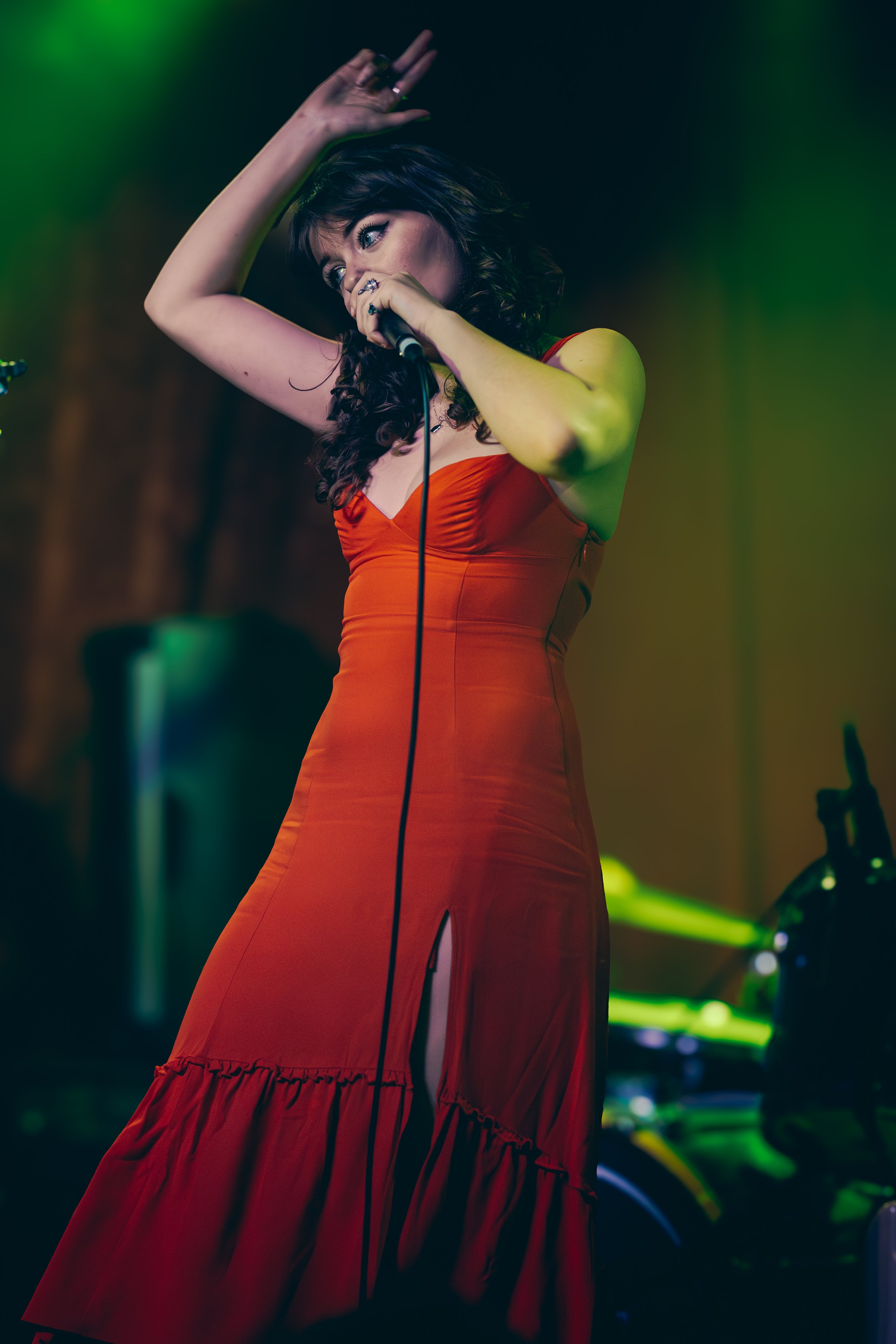 A woman in a red dress singing into a microphone on stage with green lighting.