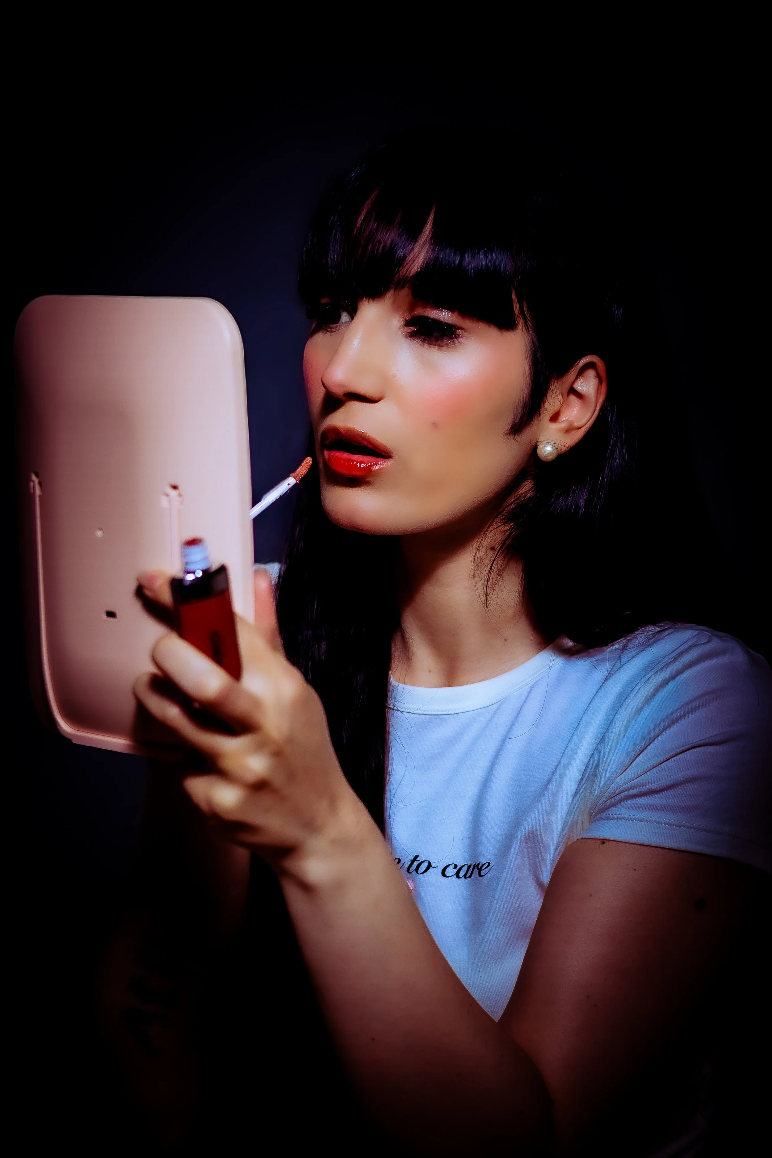 Woman applying lipstick while looking into a mirror.