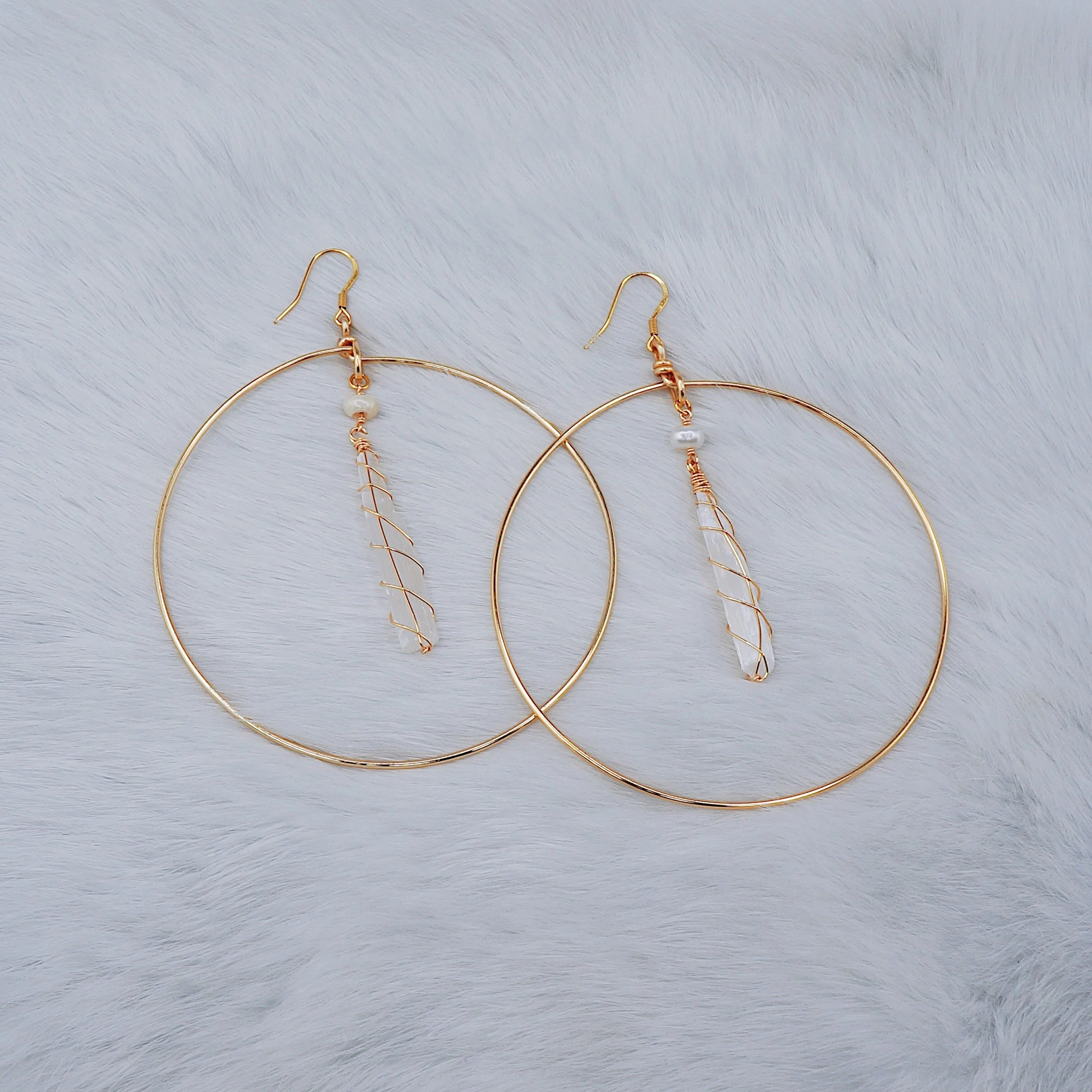 Gold hoop earrings with dangling white beads and clear pendants on a soft white fur background.