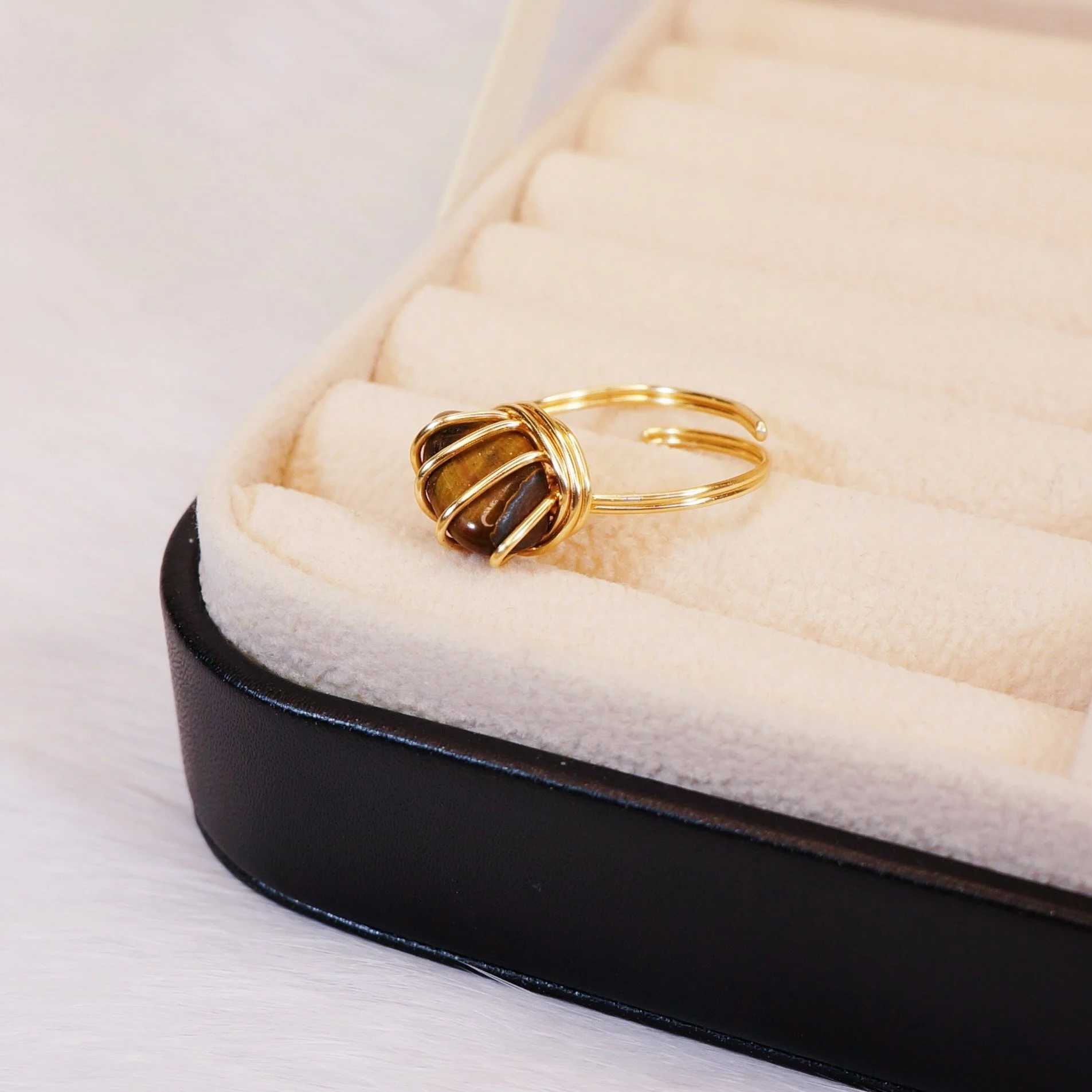 Gold ring with a large, round brown and gold stone wrapped in gold wire, displayed in a beige jewelry box.