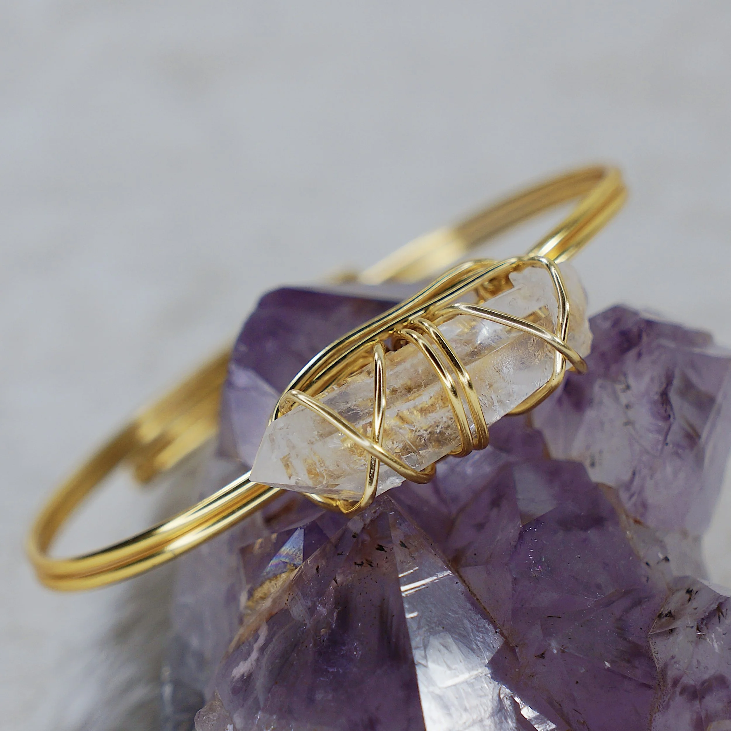 Close-up of gold jewelry with a clear stone, resting on purple quartz crystals.