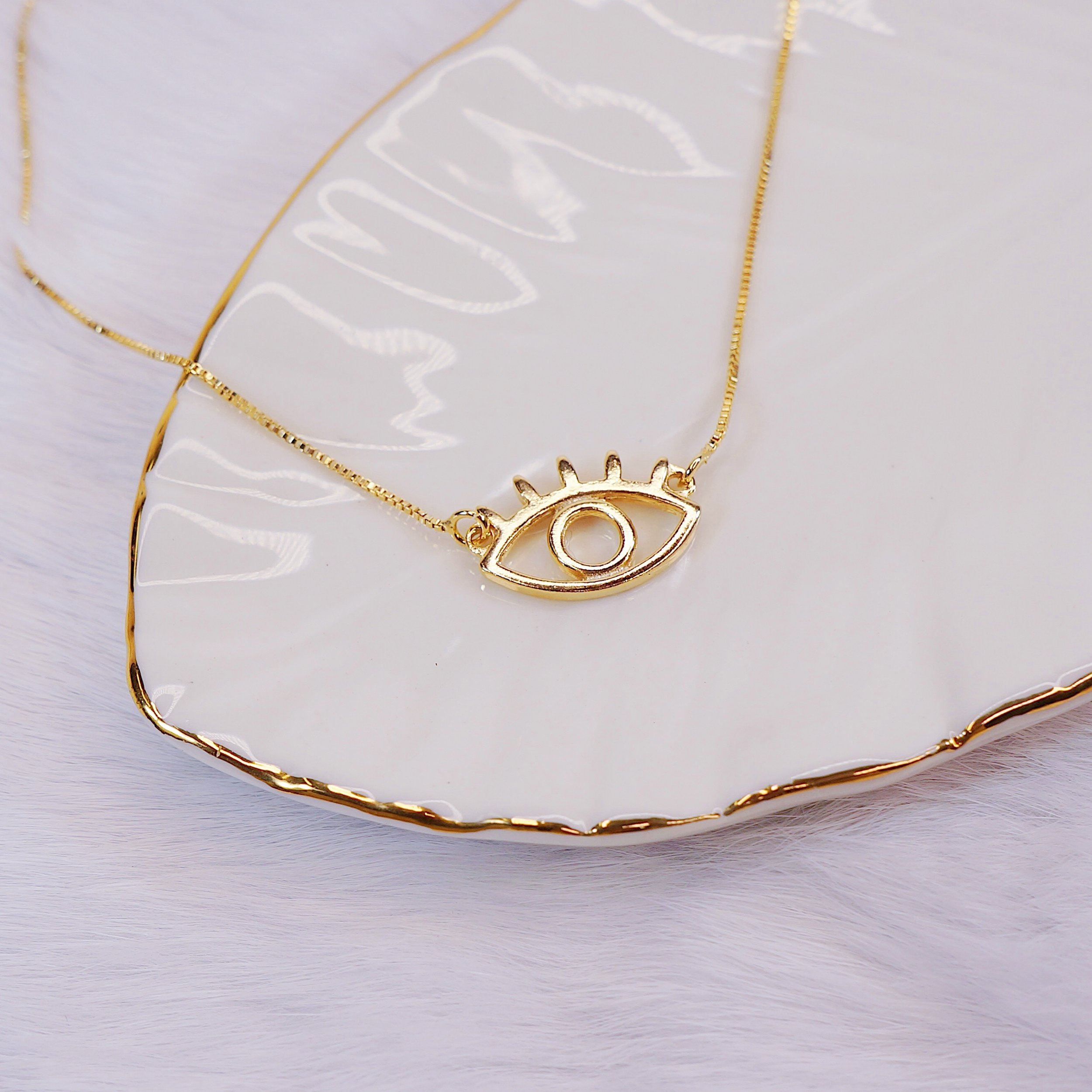 Gold eye-shaped necklace with a circular center, resting on a white plate with gold-rimmed edges.
