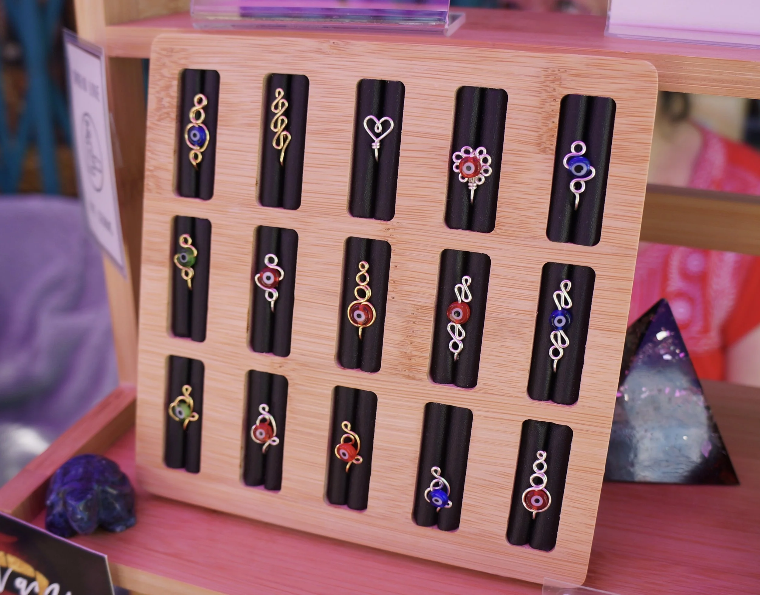 Display of colorful wire rings with various designs on a black foam stand, placed on a wooden surface.