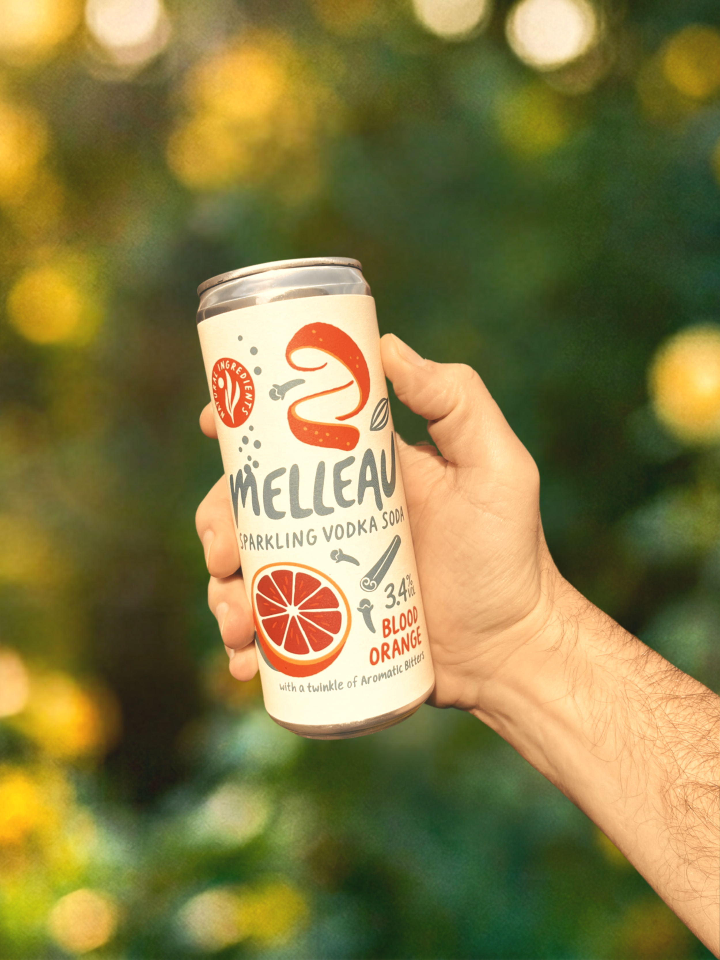 A hand holding a can of Melleau Sparkling Vodka Soda with blood orange flavor, featuring a red blood orange slice on the can and an orange peel illustration, against a blurred green and yellow background.