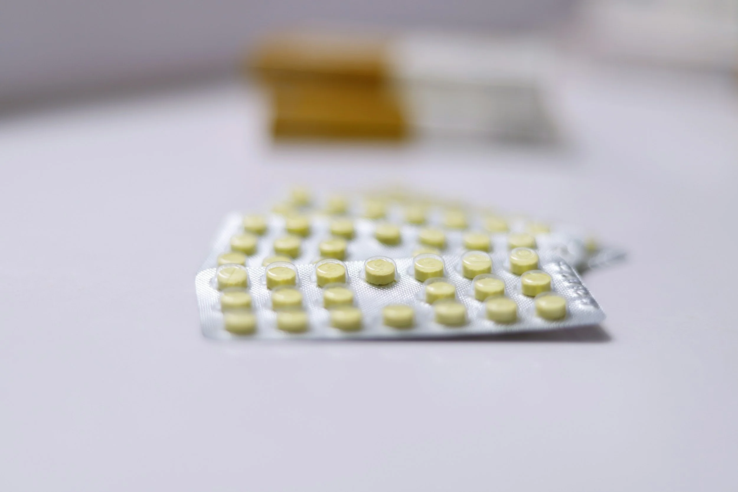 Close-up of yellow pills in blister packs on a white surface with blurred boxes in the background.