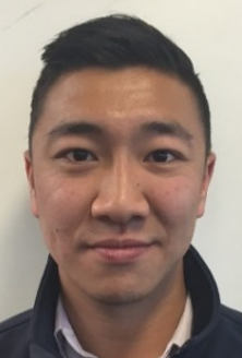 Close-up portrait of a young man with short black hair, wearing a dark jacket, smiling softly.
