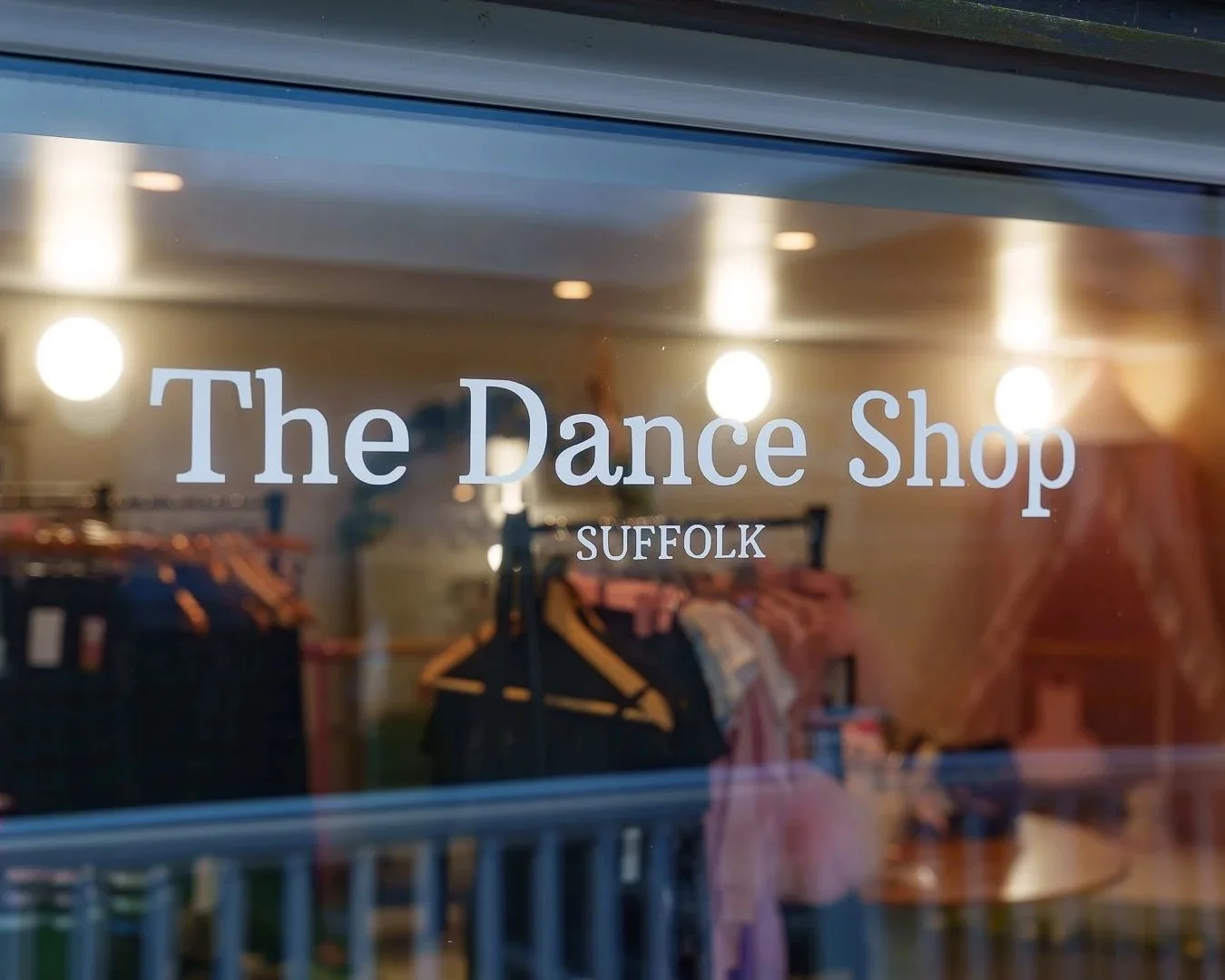 The window of The Dance Shop in Suffolk shows some clothing racks and costumes inside.