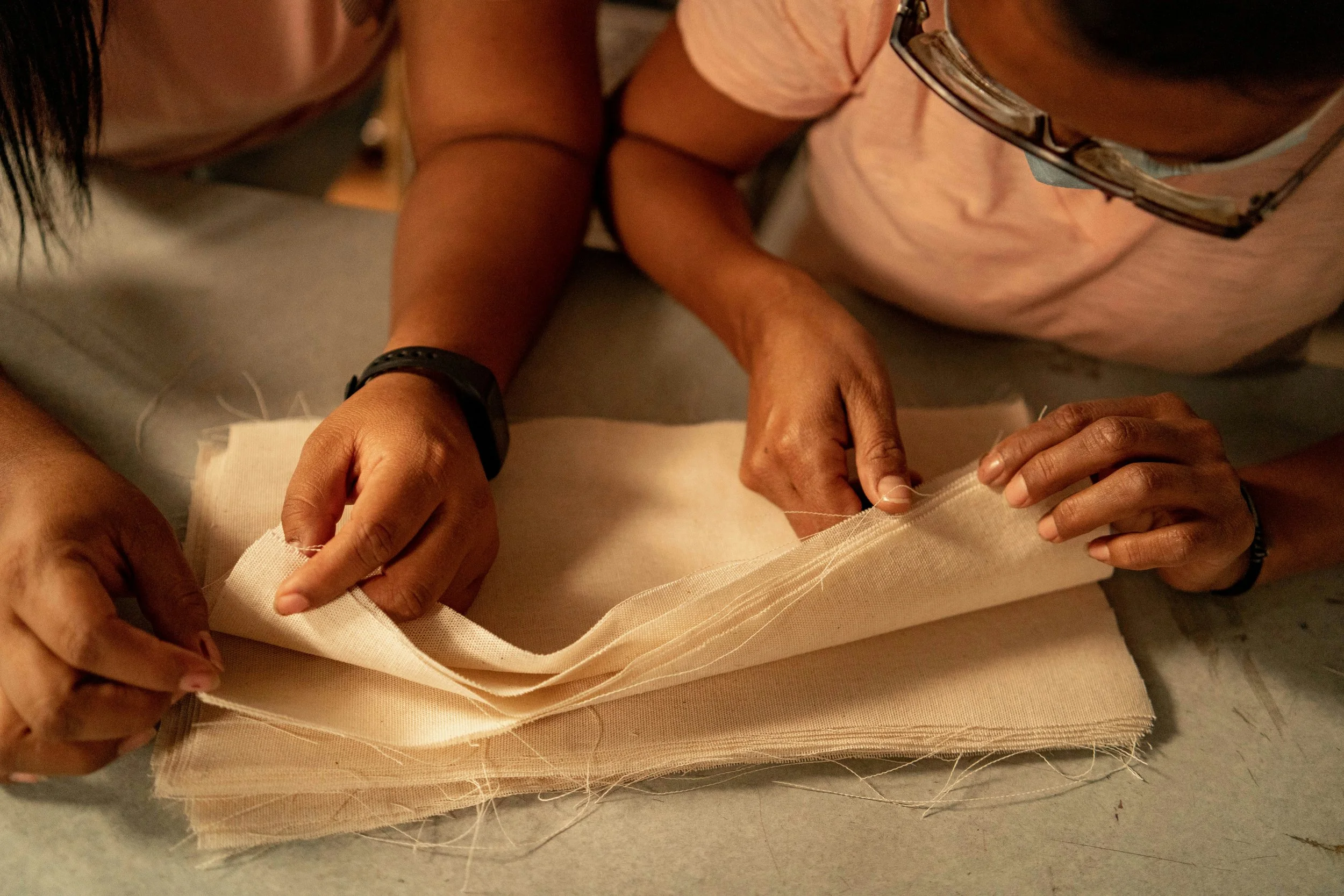 Hands working with layers of light-coloured fabric.