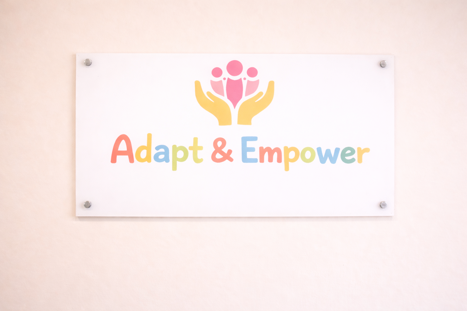 Sign with the words 'Adapt & Empower' in colorful letters and a graphic of hands holding three pink human-like figures.