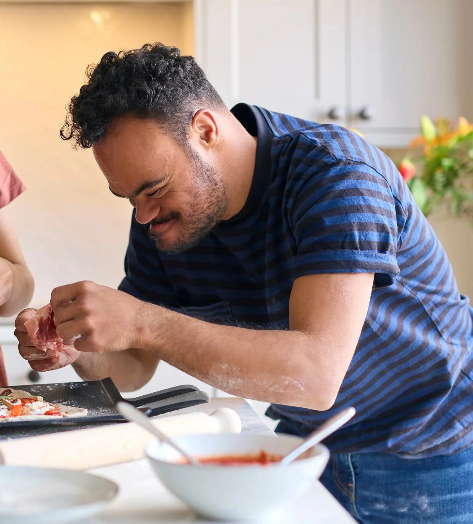 A man preparing food in a kitchen, smiling and focused on his task.