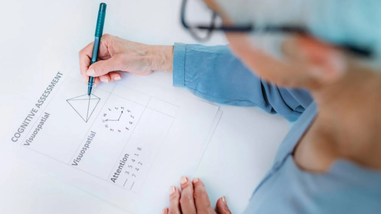 A person wearing glasses and a blue long-sleeve shirt completing a cognitive assessment test on paper with a blue pen.