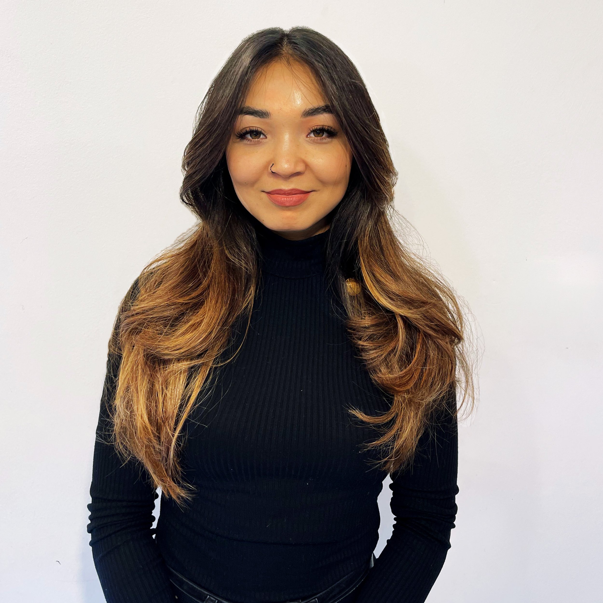 A woman with long wavy hair standing against a plain white wall.