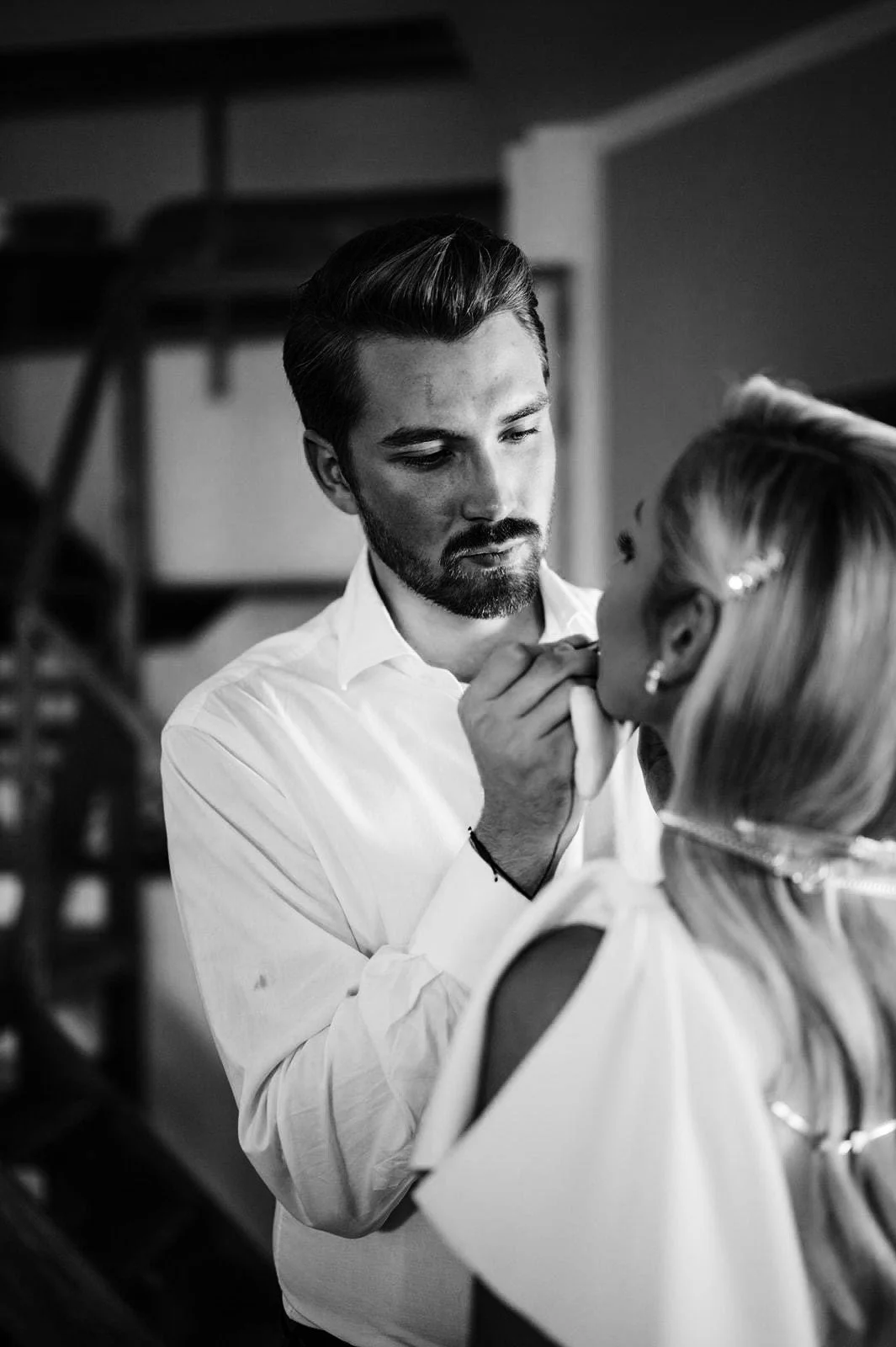 A man applying makeup to a woman, with a focus on their faces, in a black and white photo.
