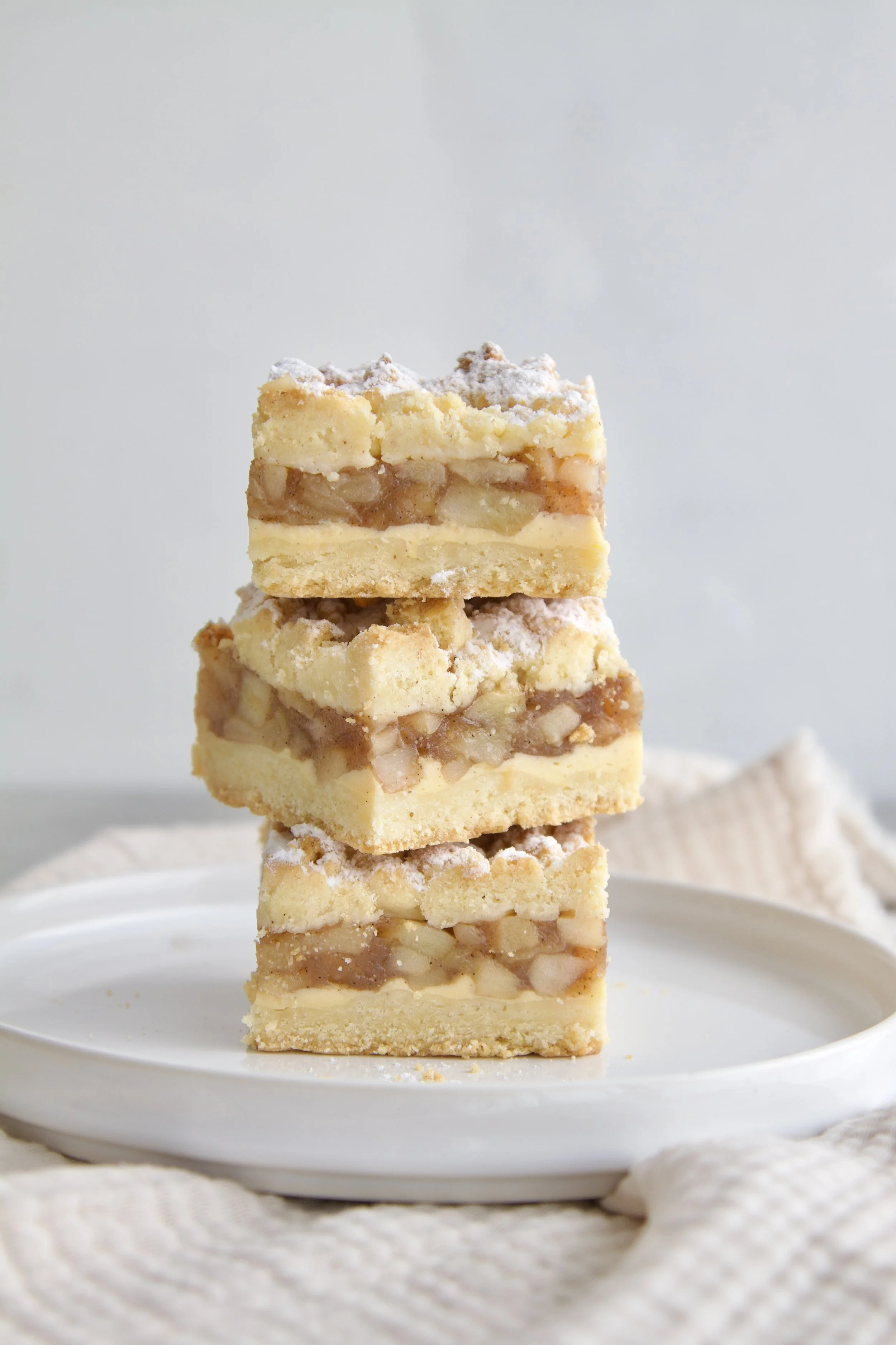 3 apple crumble cake bars stacked on top of each others where you can see the layers of crunchy crumble, vanilla pastry cream and cinnamon apple filling