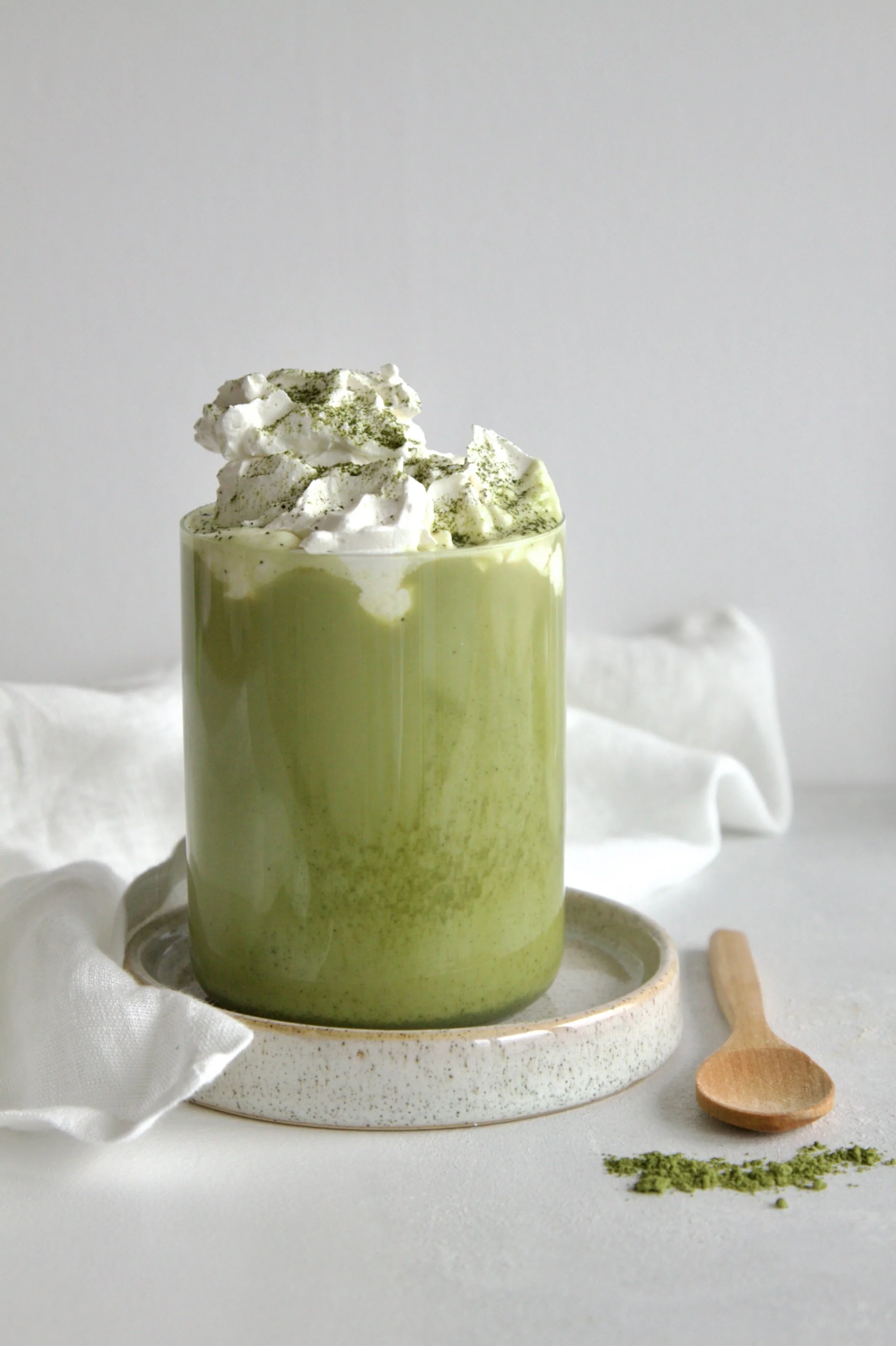 glass with green pistachio matcha latte topped with cream on top and dusted with matcha powder