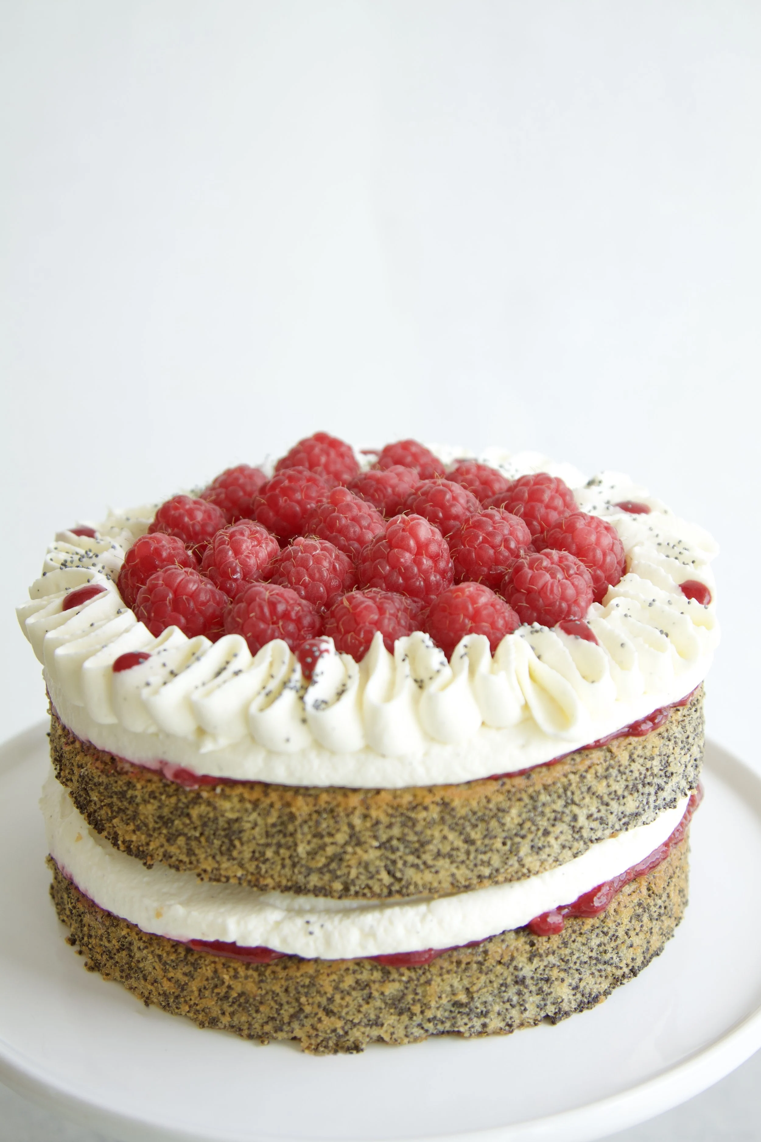 raspberry poppyseed layer cake with visible layers, fresh raspberries and mascarpone cream piping