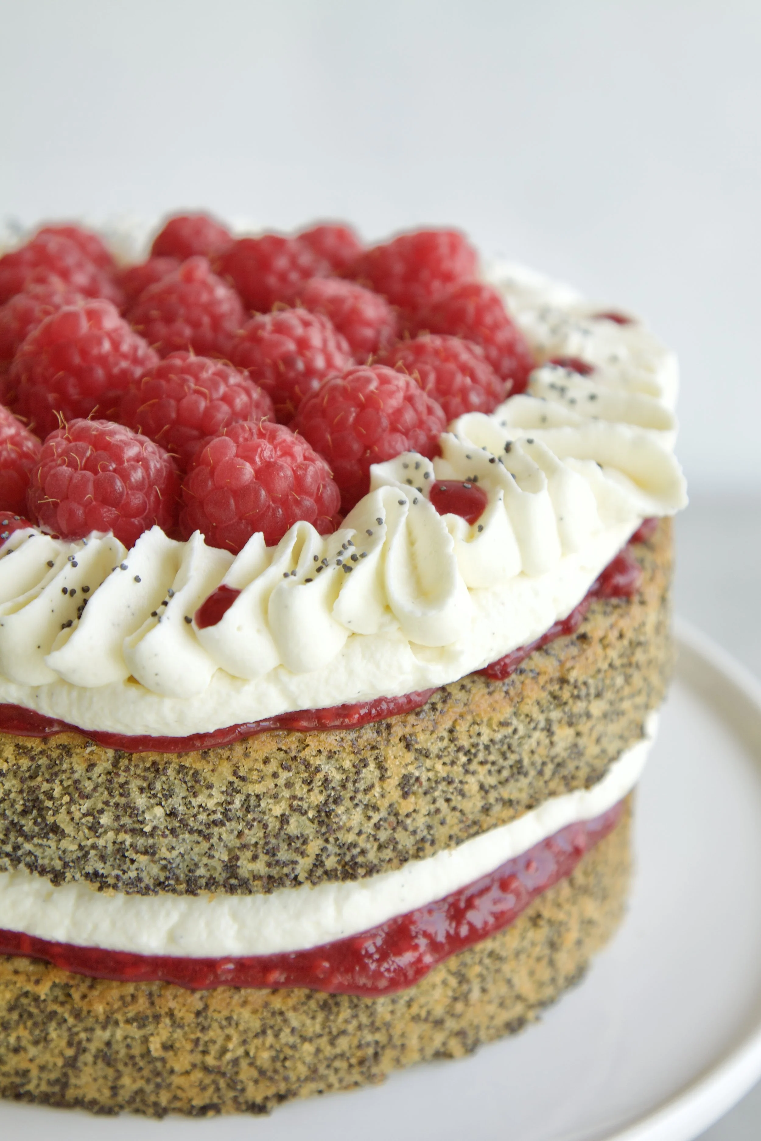 raspberry poppyseed layer cake with visible layers and topped with fresh raspberries and mascarpone cream piping