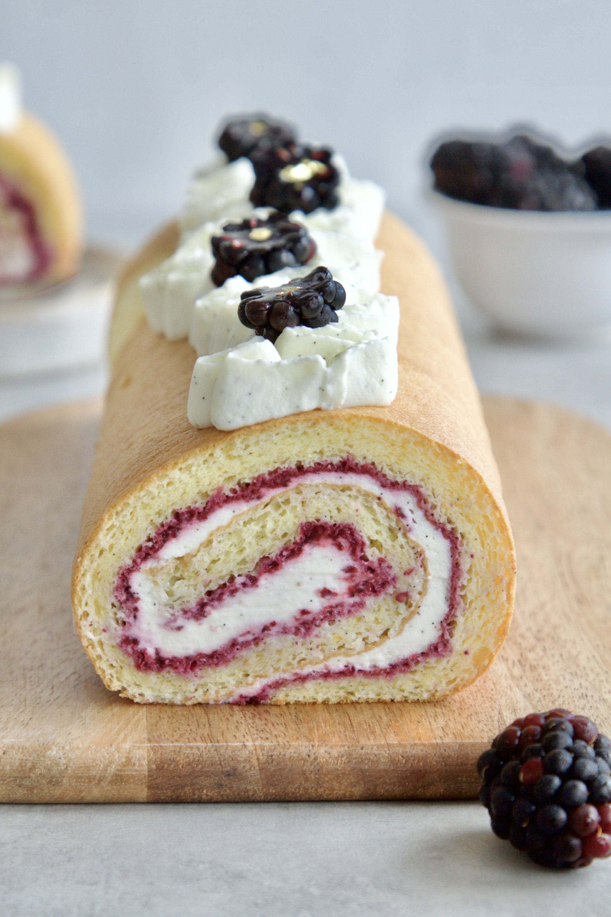 Log with a cut so you see the inside of a blackberry vanilla Swiss roll cake with the swirled fillings visible