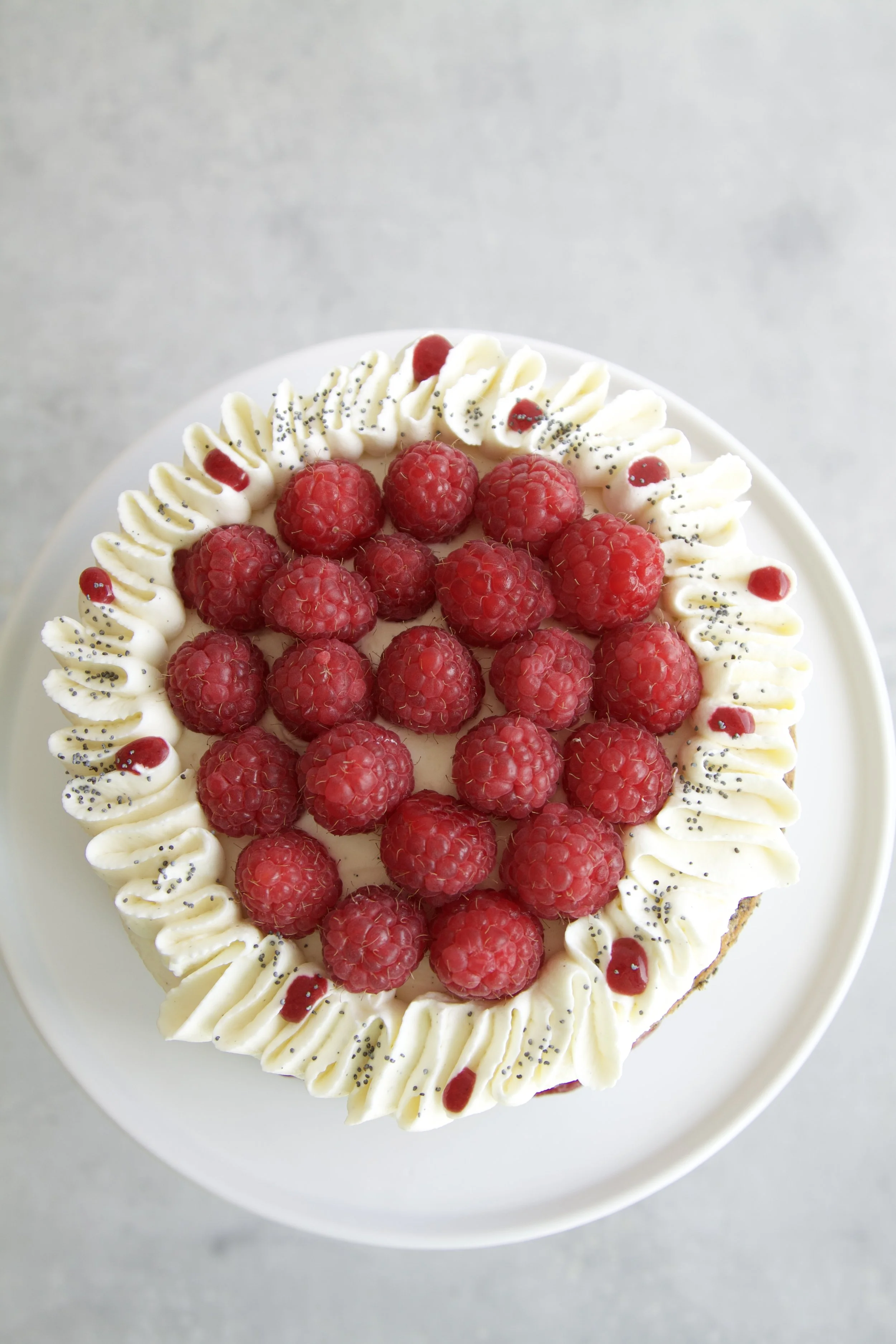 top view of a raspberry poppyseed layer cake with mascarpone cream and fresh raspberries on top