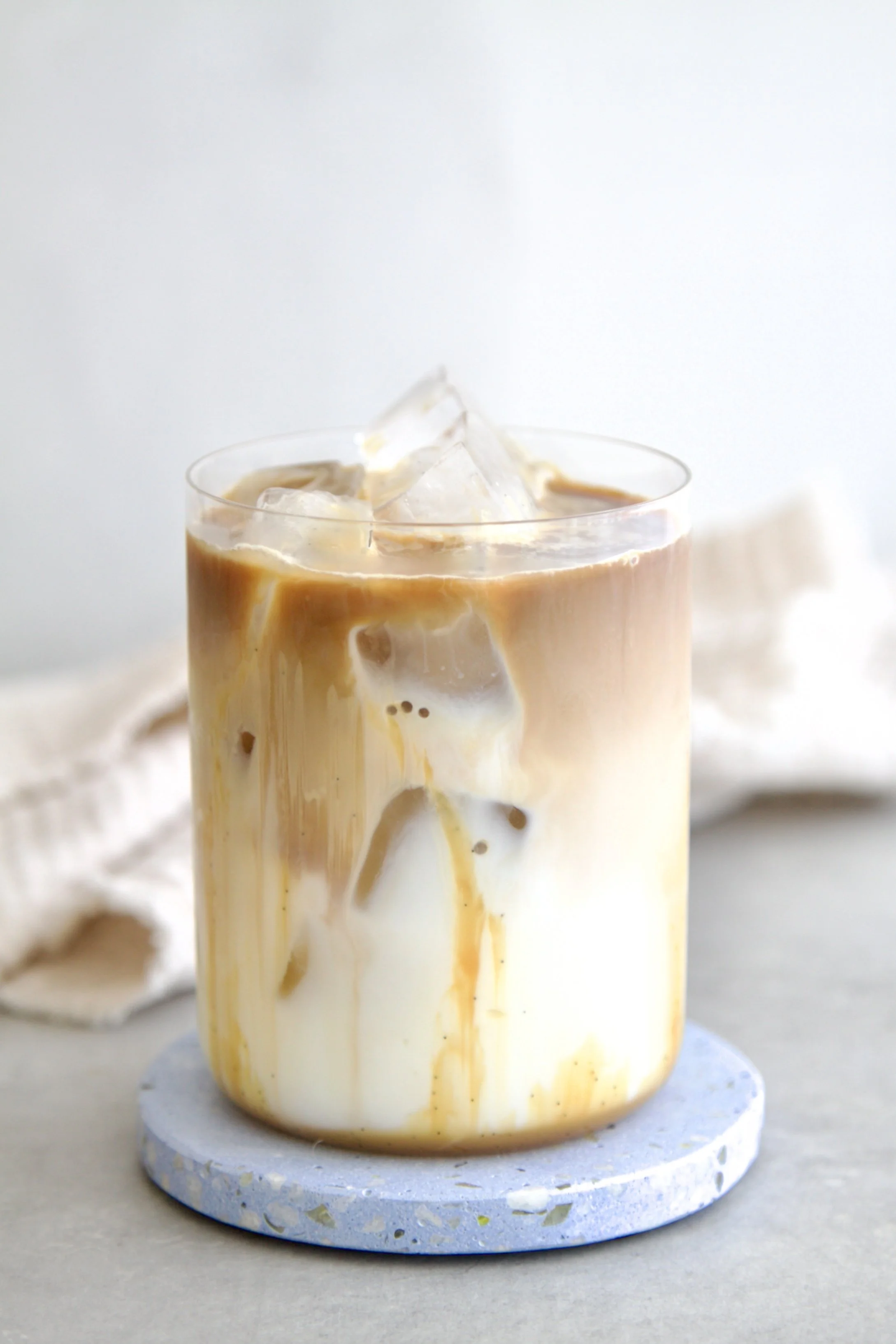 glass filled with an iced vanilla caramel coffee where you can see the caramel sauce, iced cubes and coffee with milk