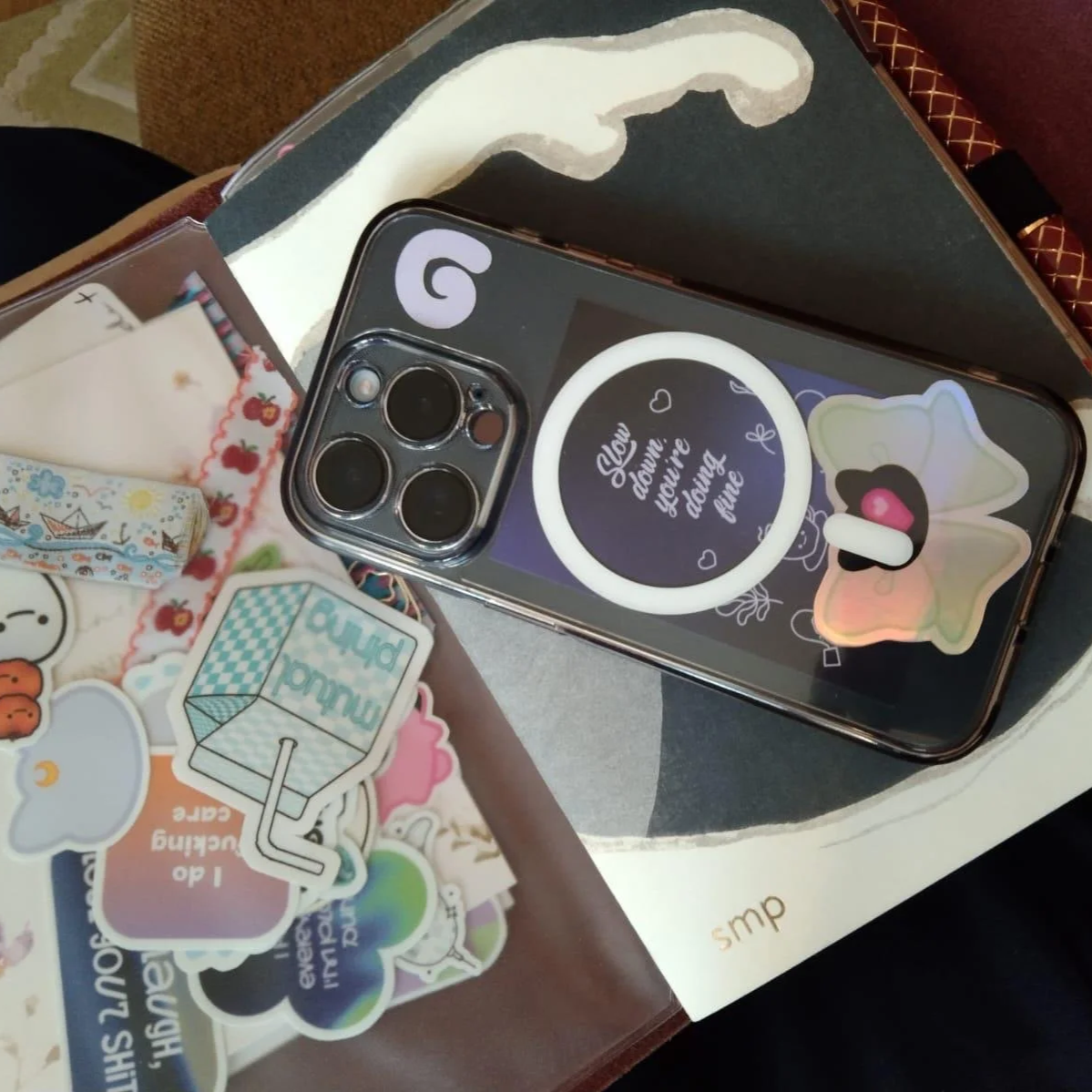 Smartphone mit einem Sticker, der sagt 'Now daɯve: you're daɯng away', und verschiedenen Aufklebern auf einem Tisch.