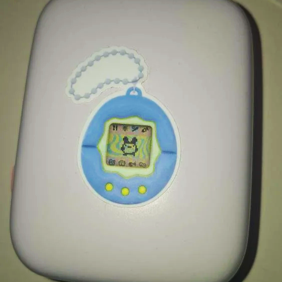 Ein blauer Tamagotchi mit einem grünen Rahmen, das an einer Kette hängt.