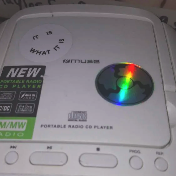 Ein tragbarer Radio-CD-Player mit einer reflektierenden CD und einem Aufkleber mit dem Text 'IT IS WHAT IT IS'.