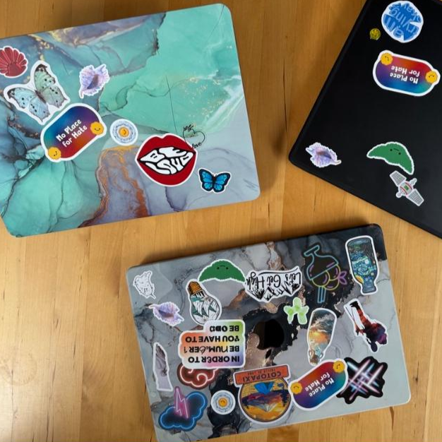 Drei MacBooks mit bunten Stickern auf einer Holzoberfläche.