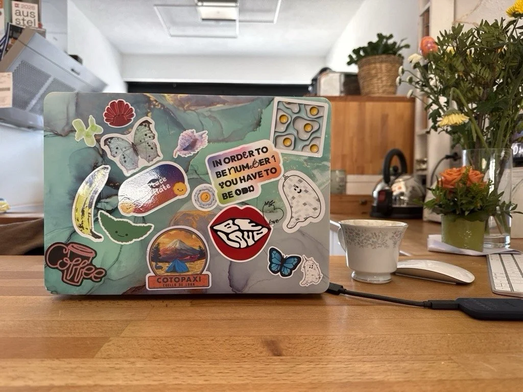 Laptop mit Sticker, Tasse, Blumen auf Tisch in Café oder Büro.