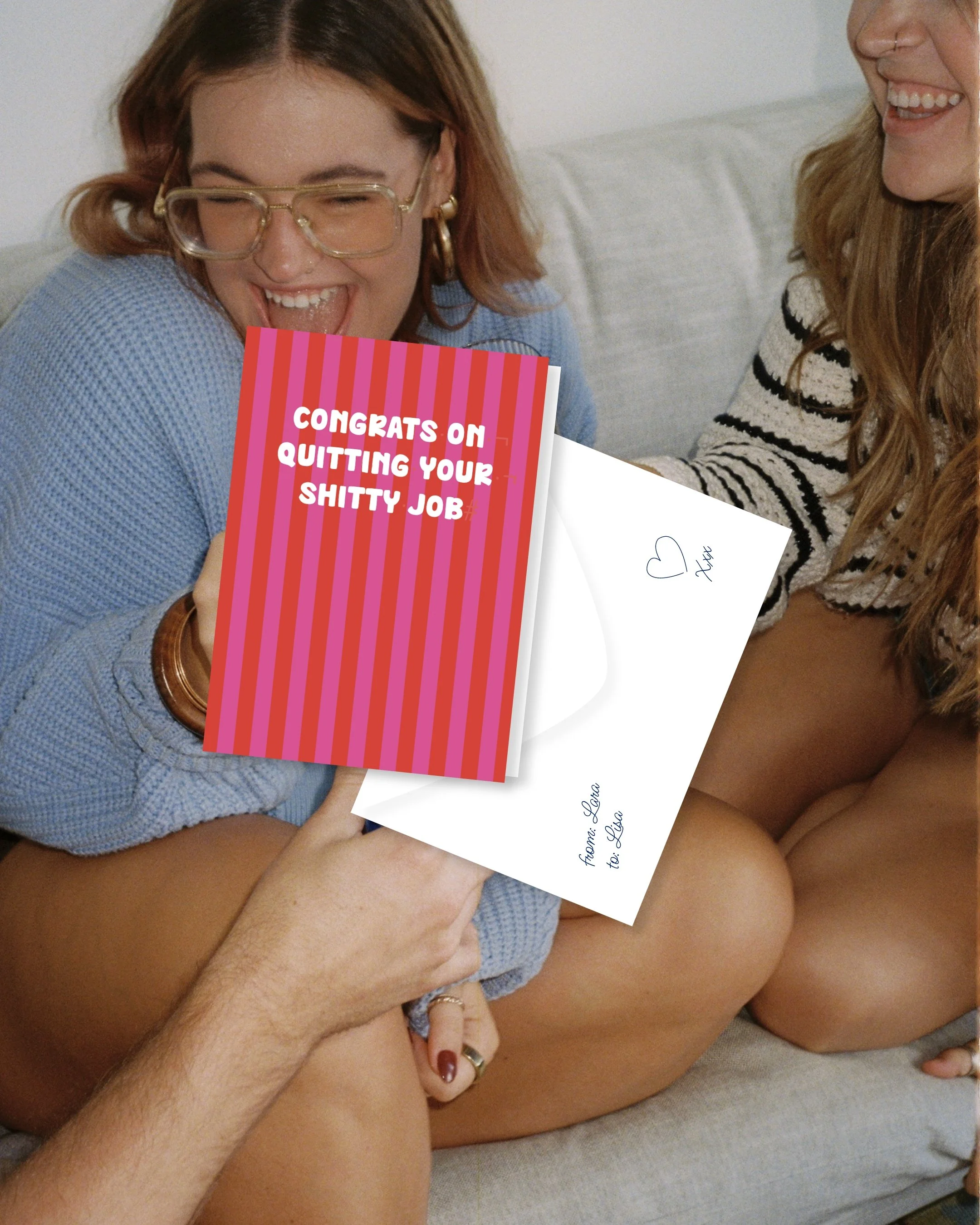 Zwei Frauen sitzen auf einem Sofa, lachen und halten eine Grußkarte in den Händen. Die Karte trägt den Text 'Congrats on quitting your shitty job'.