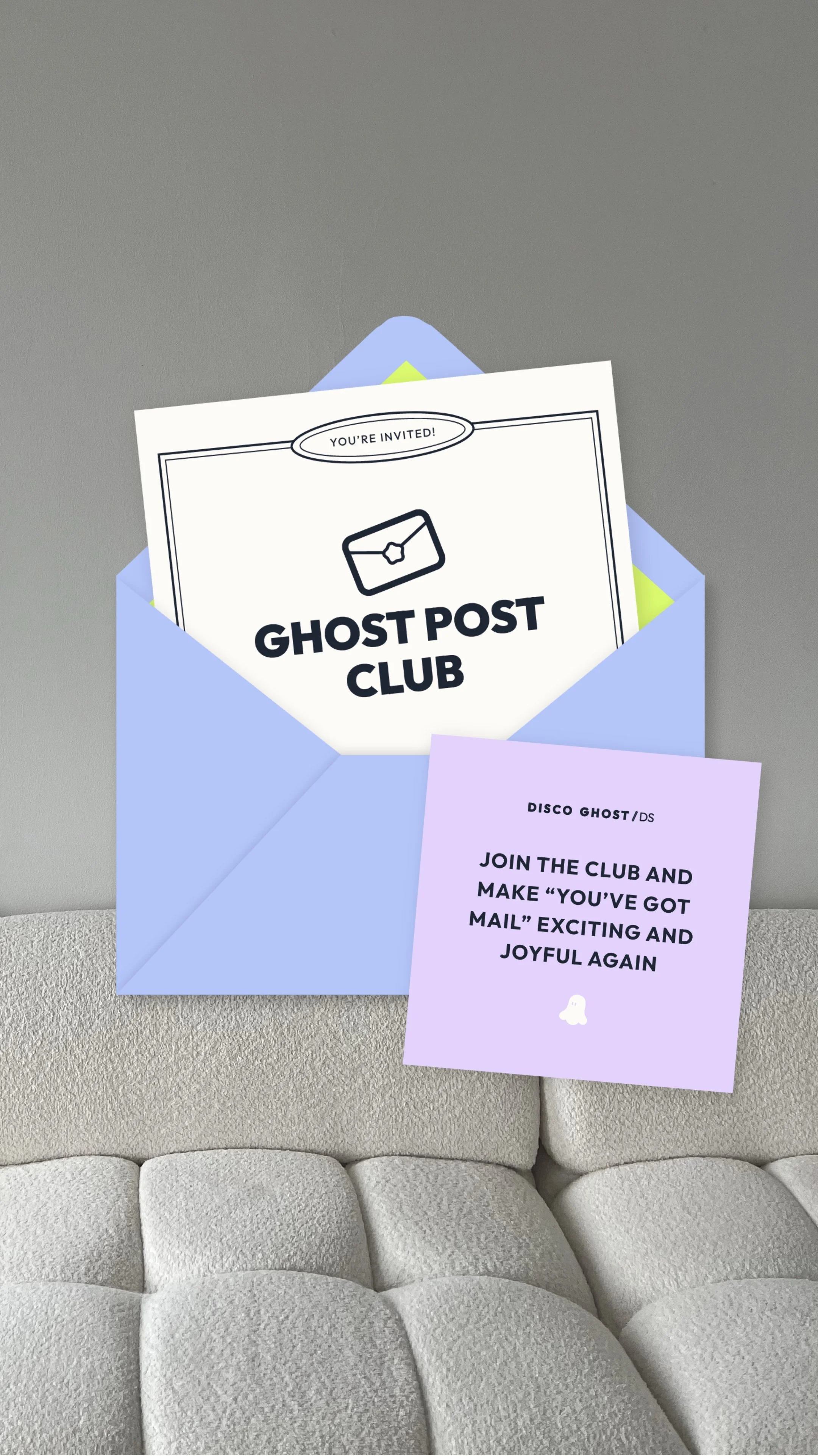 Ein blauer Briefumschlag mit einer Einladungskarte in einem grauen Raum auf einem grauen Sofa. Die Einladung trägt den Titel 'GHOST POST CLUB' und enthält ein Symbol für einen Briefumschlag. Ein zusätzliches lila Kärtchen mit Text lädt dazu ein, dem Club beizutreten, um wieder Freude am Mail-Schreiben zu finden.