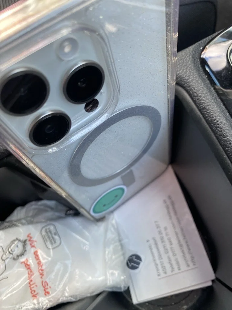 Ein Gerät mit drei runden schwarzen Öffnungen und einem grünen Knopf liegt in einem Auto, neben einer Papierscheibe und Dokumenten.