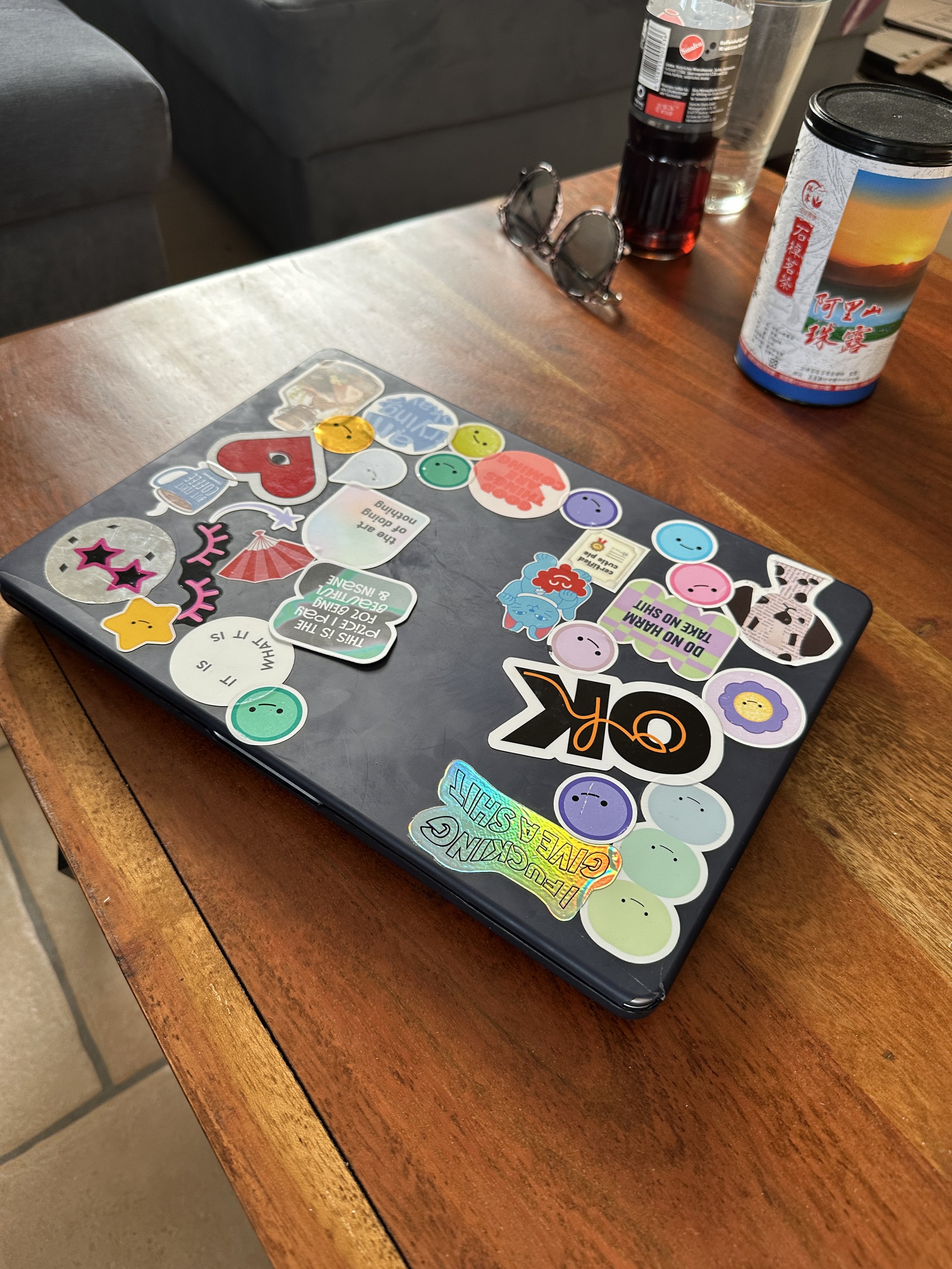 Ein Computer mit Aufklebern auf einem Holz Tisch, im Hintergrund Getränke, eine Brille, eine Wasserflasche und eine Dose. Die Aufkleber tragen lustige und motivierende Sprüche und Symbole.