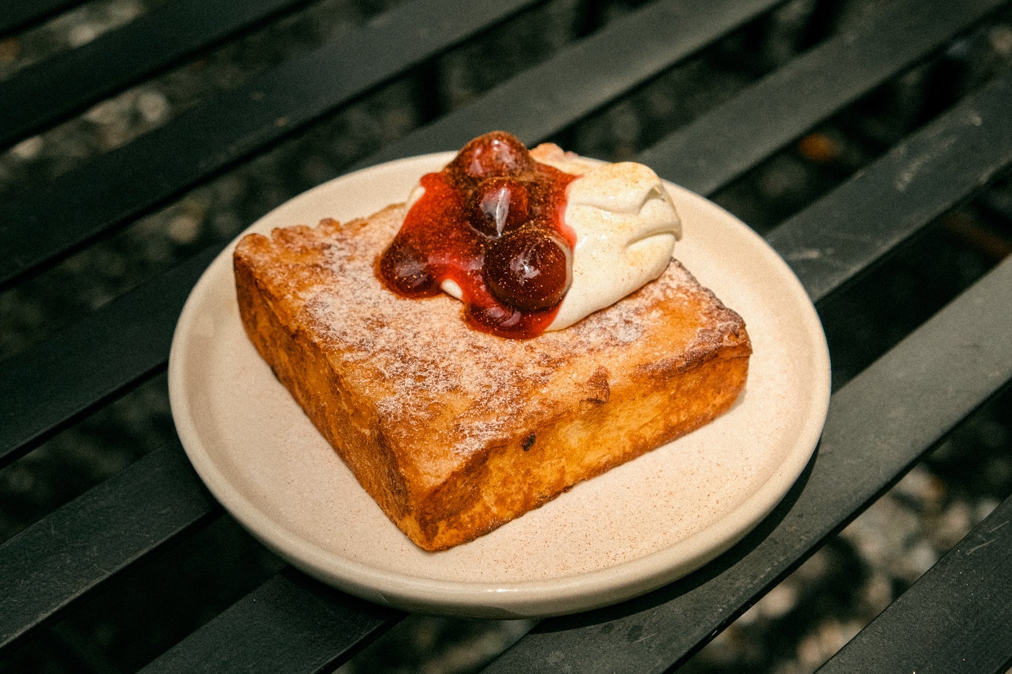 A slice of French toast topped with whipped cream and cherry syrup on a white plate.