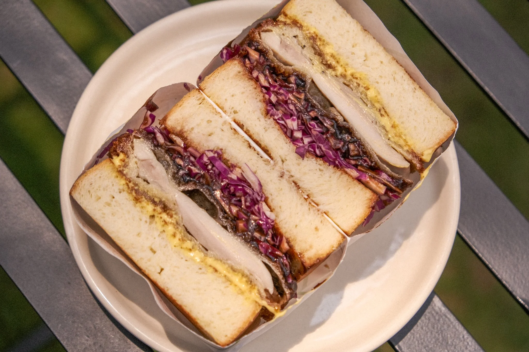 A plate with three sandwich halves filled with fried chicken, purple cabbage, and sauce, served on white bread.