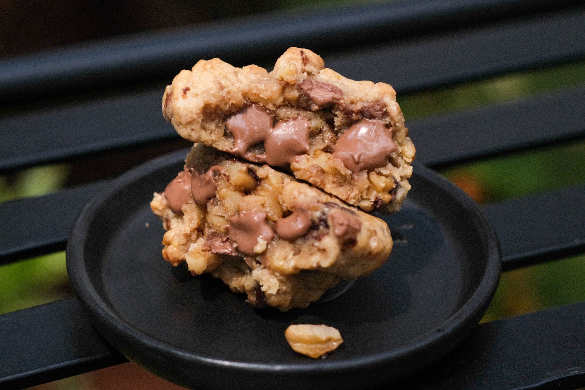 Close-up of a chocolate chip cookie stacked on a black plate on a black slatted surface.