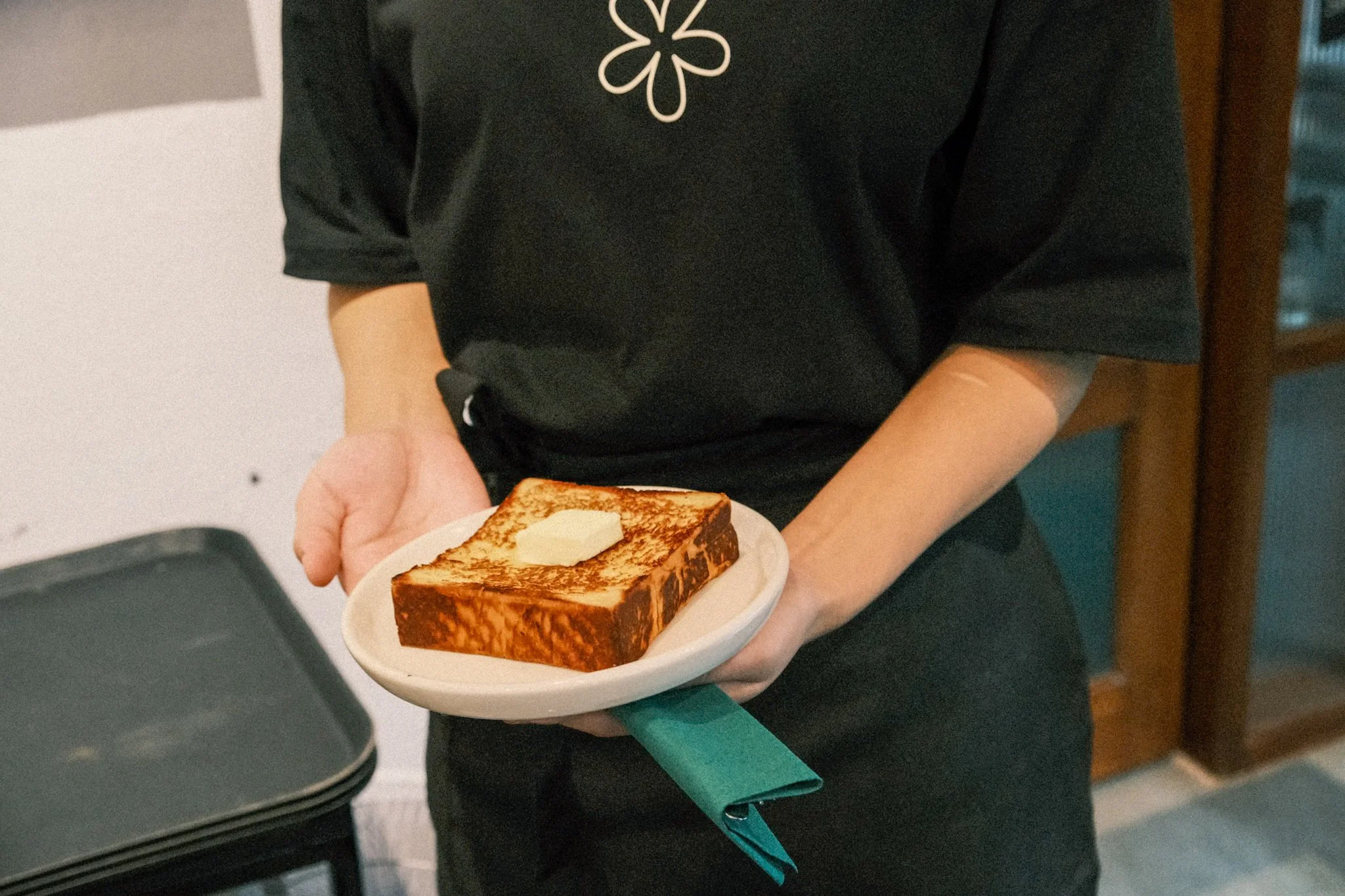 Person holding a plate with a thick slice of toasted bread topped with butter.