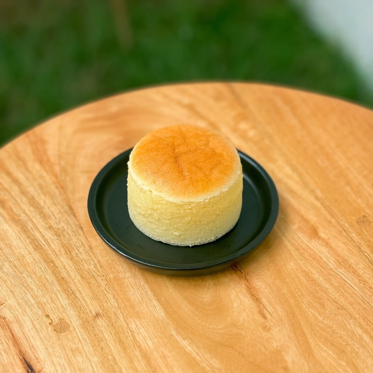 A single Japanese cheesecake on a small black plate, placed on a wooden table.