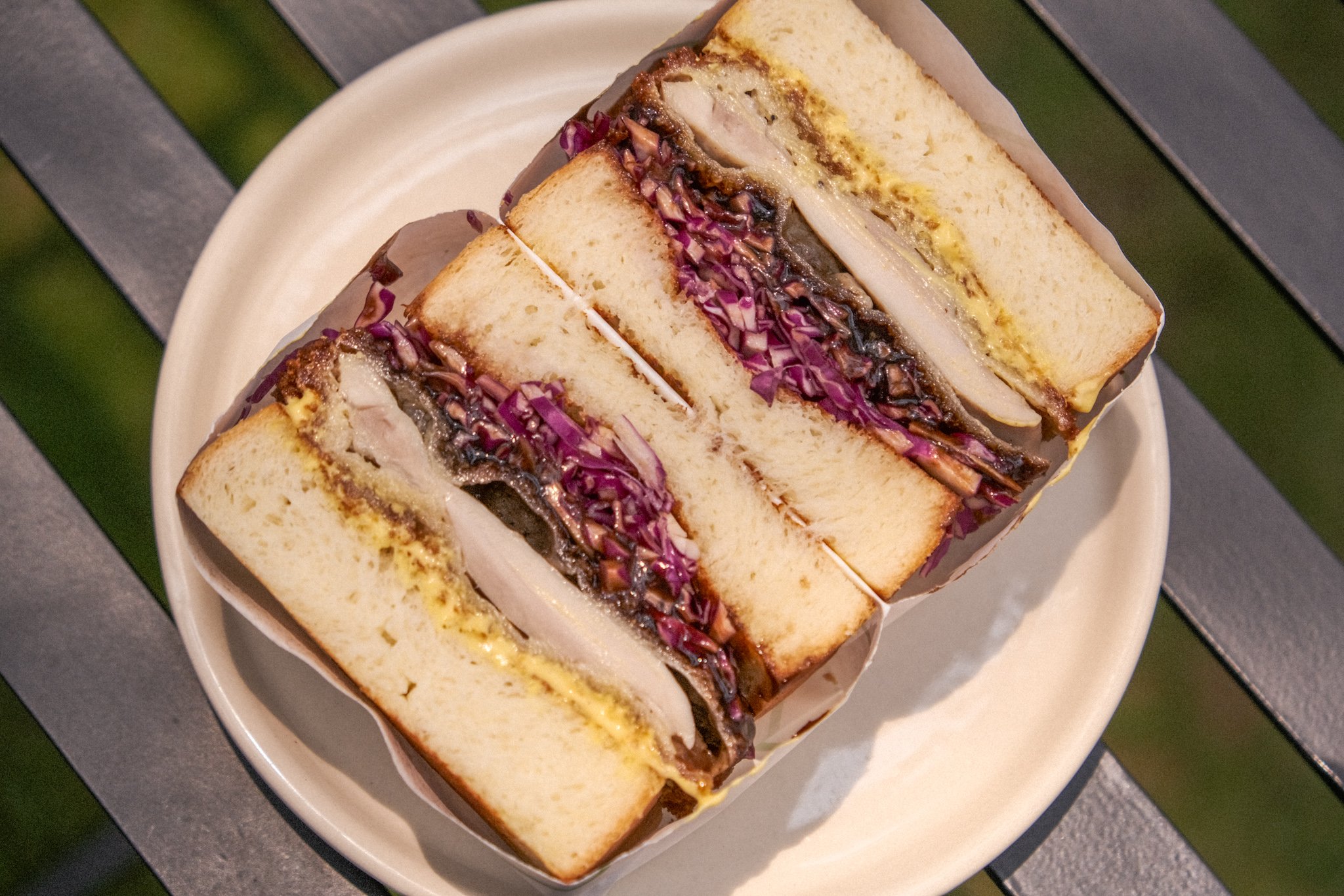 Close-up of two chicken sandwiches with purple cabbage slaw, pickles, and mayonnaise, served on white bread with crusts removed.