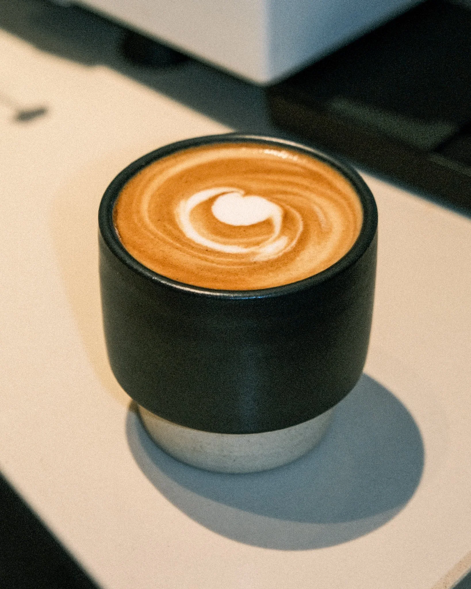A cup of coffee with latte art in a black ceramic mug on a white table.