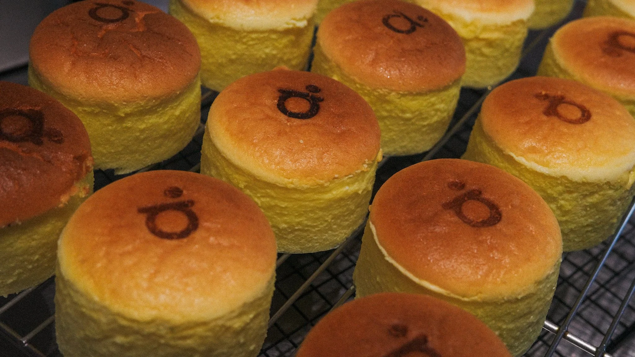 Close-up of freshly baked, round, golden-brown bread rolls with a few marked with a number on top, cooling on a wire rack.