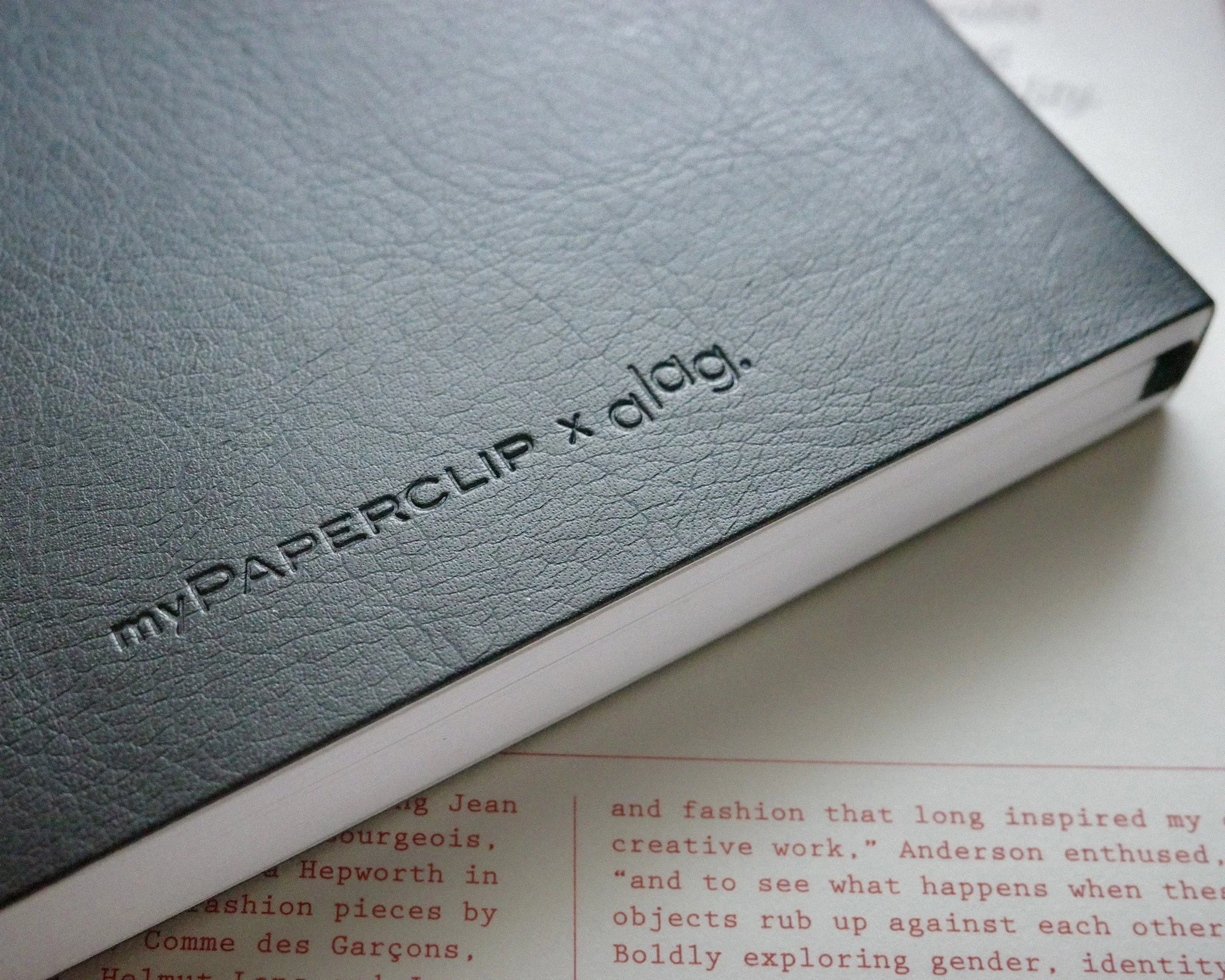 Close-up of a black textured notebook cover with the words "my PAPERCLIP x dladg." embossed on it.