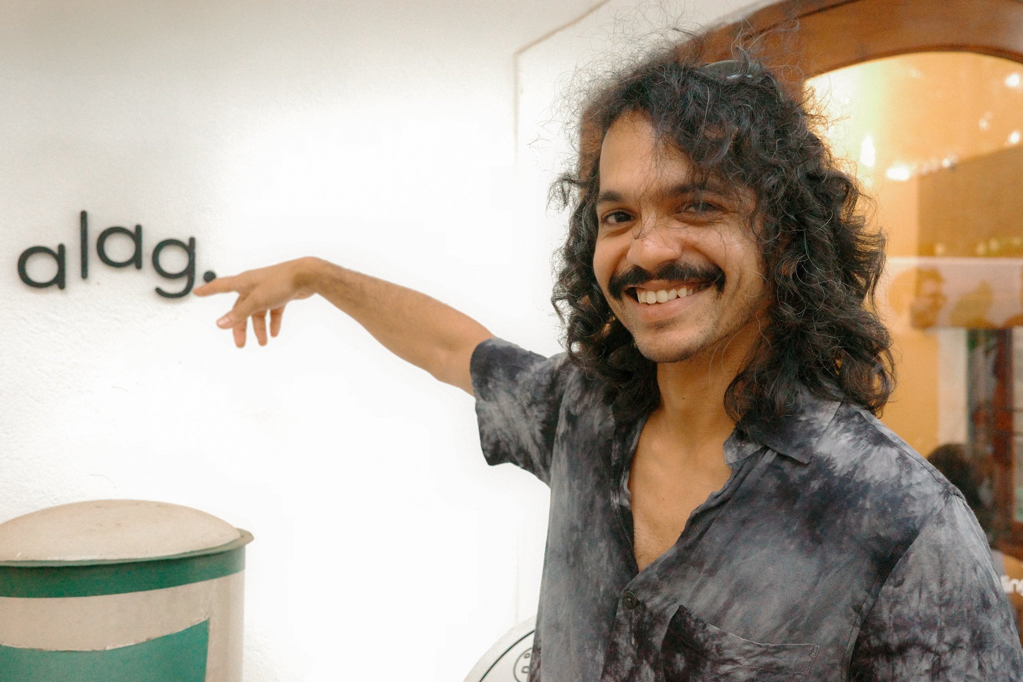 Man with curly hair and a mustache smiling, pointing at a wall with the word 'a dog.'